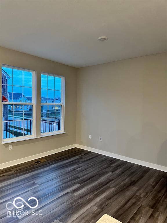 Neutral-toned room featuring dark-stained wood-finish flooring and dual windows with multi-pane grilles