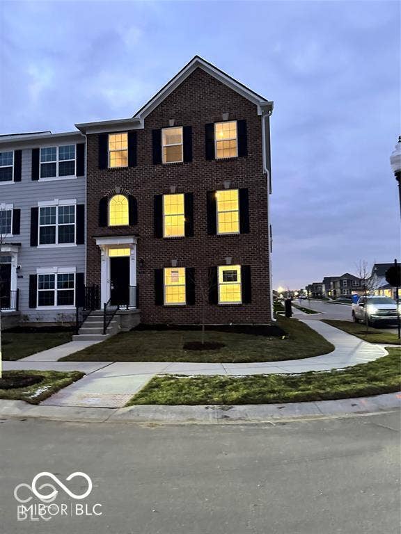 Three-story brick exterior featuring a covered entryway, decorative shutters, an arched window, and a concrete walkway