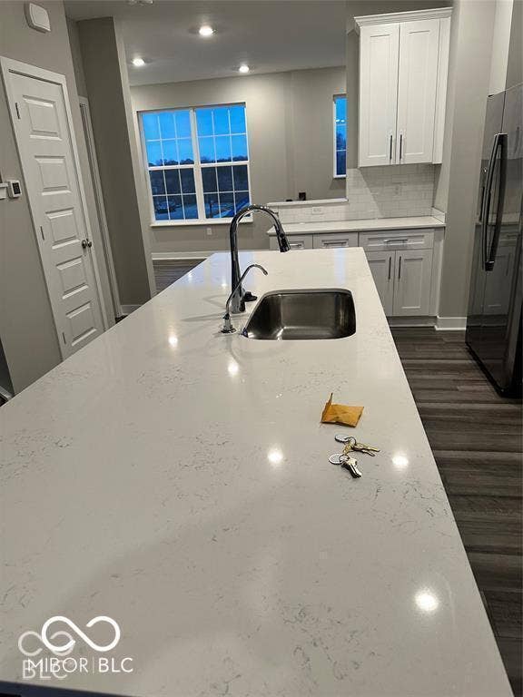 Kitchen island featuring a white surface with subtle grey veining, a stainless steel undermount sink, a gooseneck faucet, white shaker-style cabinetry, and wood-finish flooring