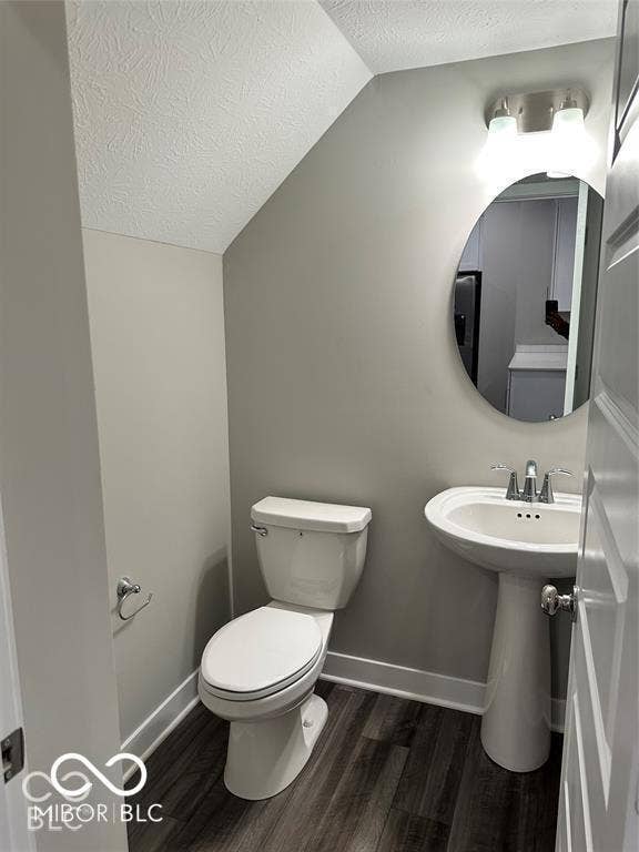 Powder room featuring a pedestal sink, polished chrome faucet, round wall-mounted mirror, and wood-finish flooring