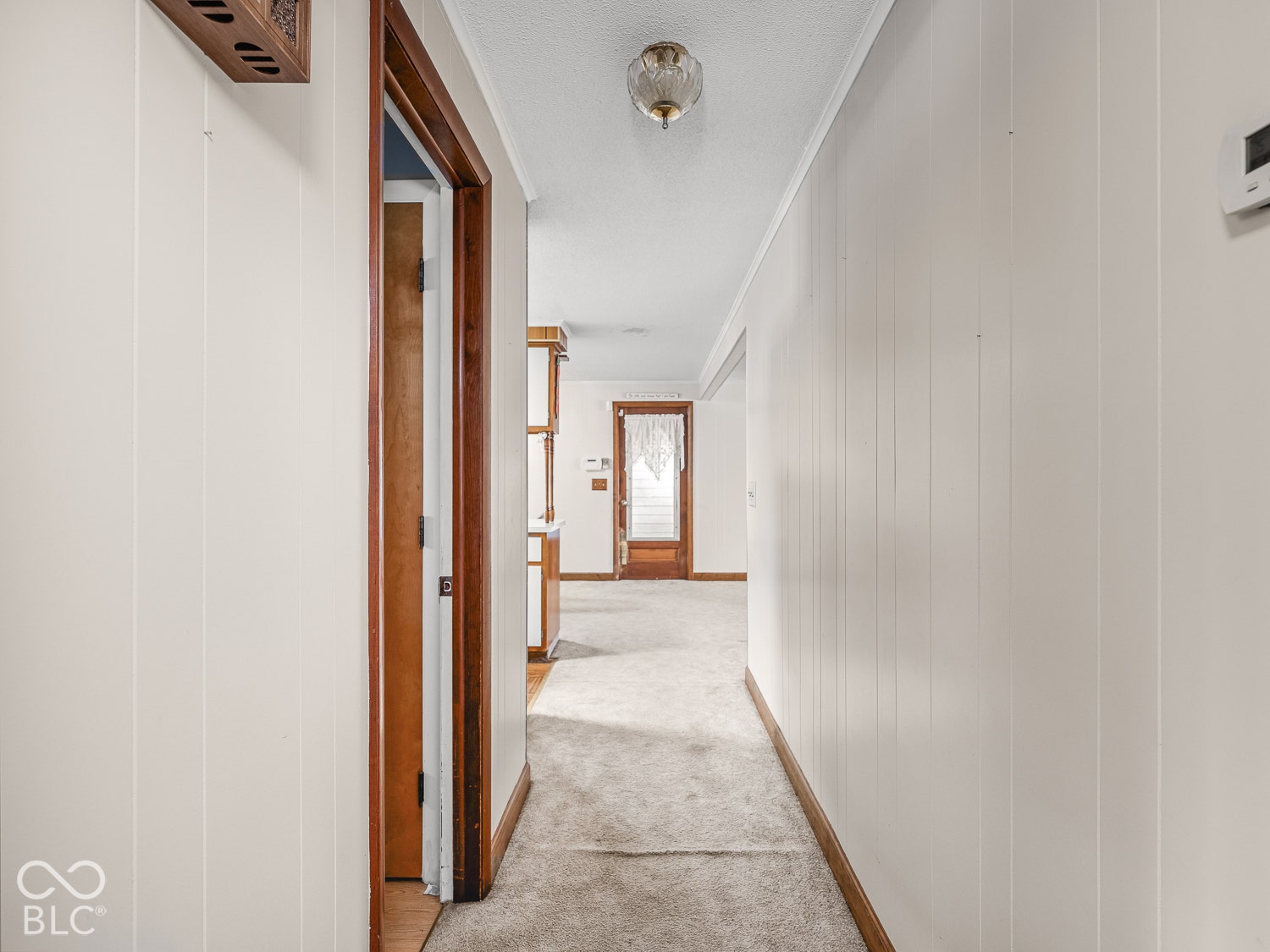Hallway featuring vertical wood paneling, wood-trimmed door frames, carpeted flooring, and a flush-mount ceiling light fixture