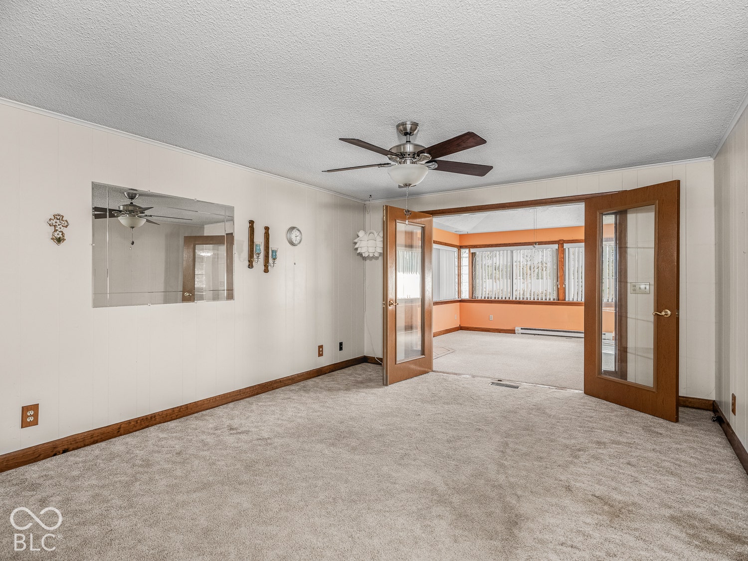 Room interior featuring wall-to-wall carpeting, wood-frame French doors, integrated wall-mounted mirror, and a ceiling-mounted light and fan fixture