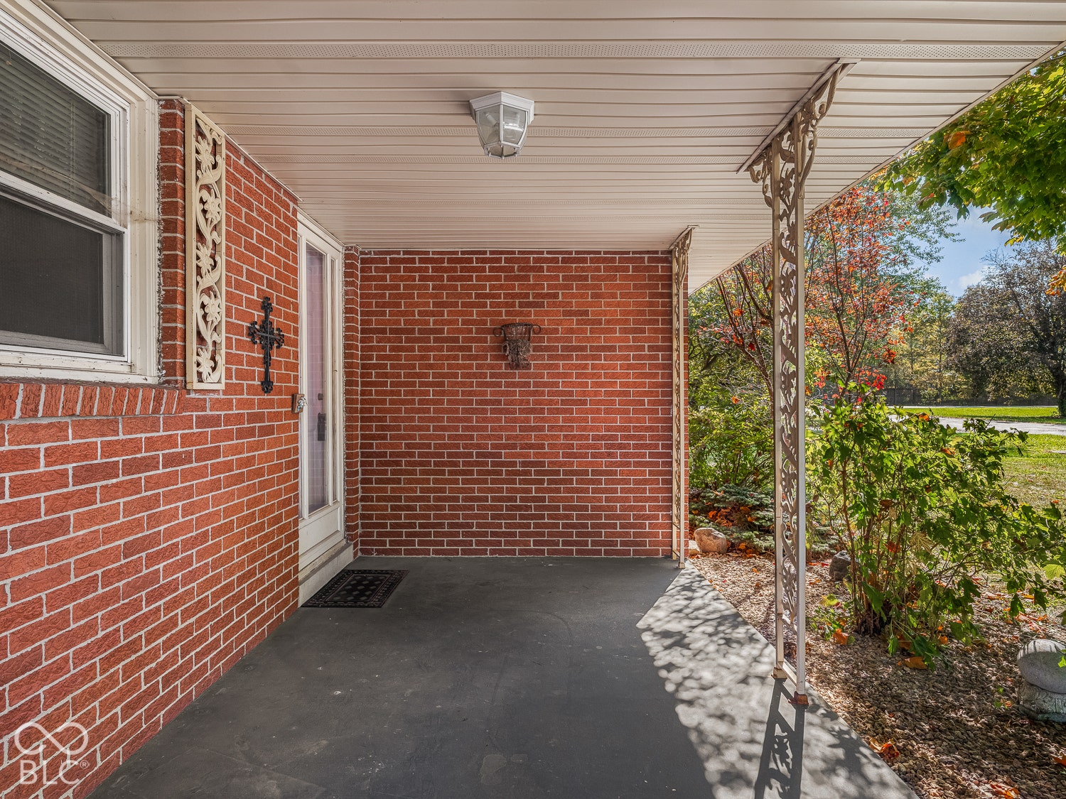 Covered front porch featuring red brick exterior siding, decorative metal columns, and a flush-mount light fixture