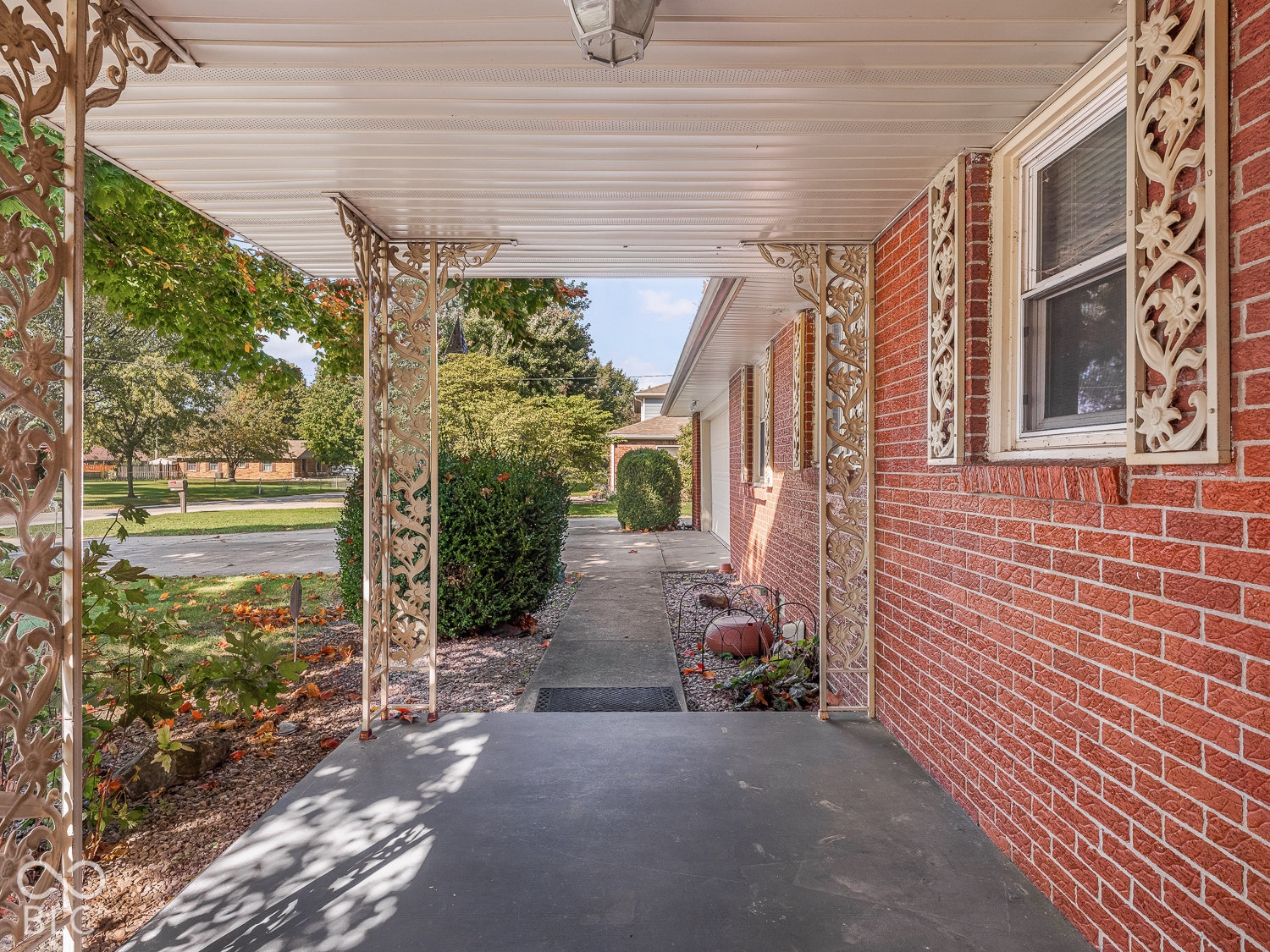 Covered entry porch featuring red brick exterior, ornate wrought iron support columns, and decorative metal shutters