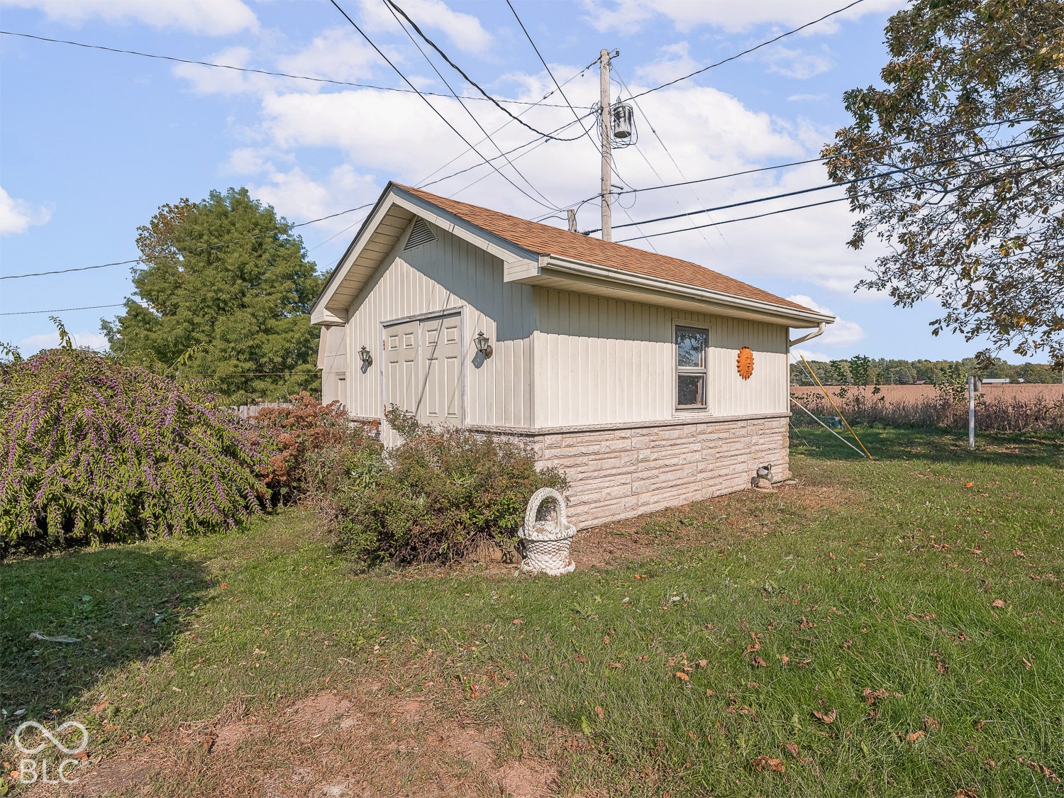 Detached outbuilding featuring vertical siding, stone-textured lower exterior, a gable roof, and electricity installed inside