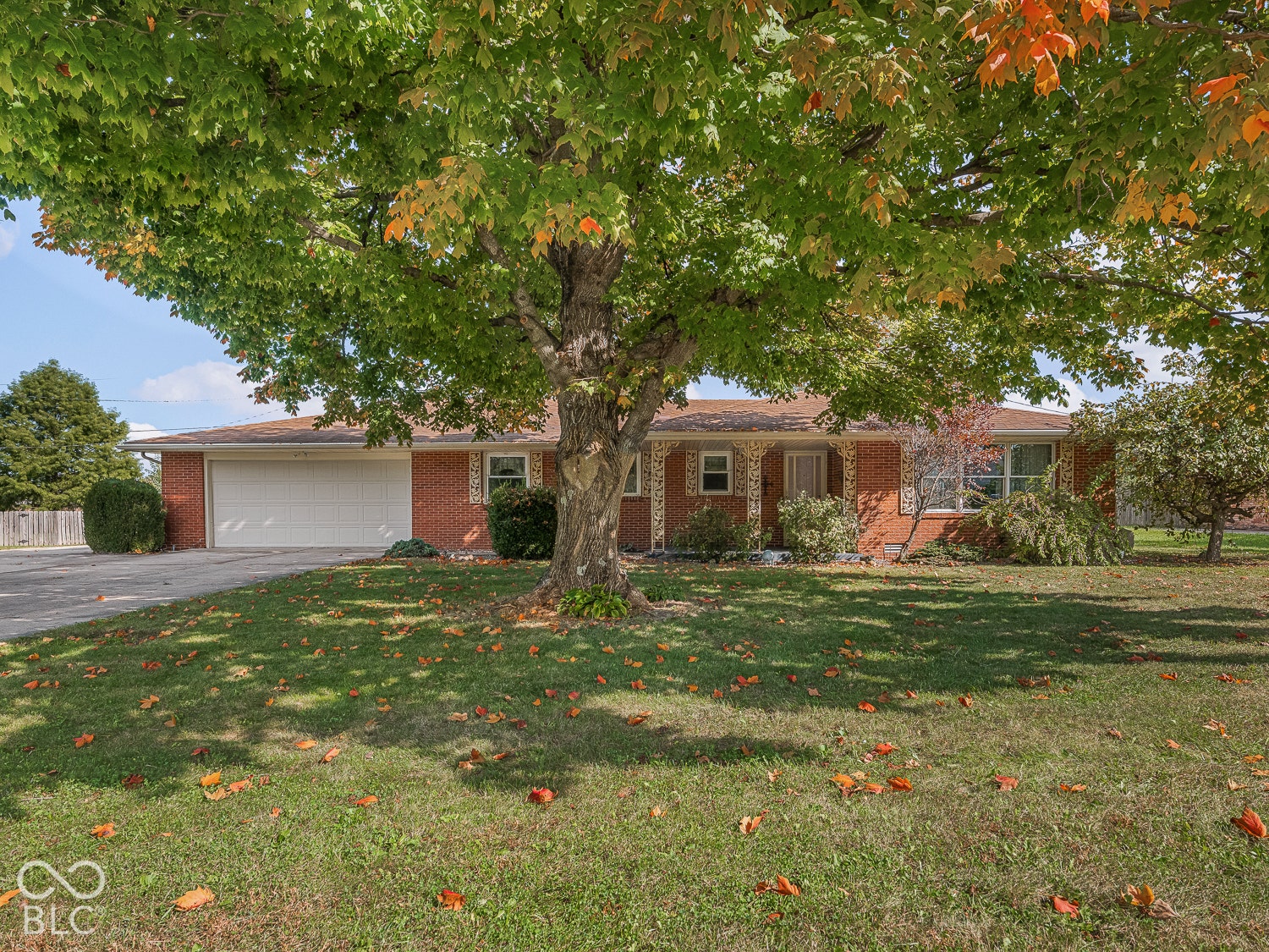 Red brick exterior featuring a multi-car garage, expanded driveway, expansive front lawn, and mature canopy trees