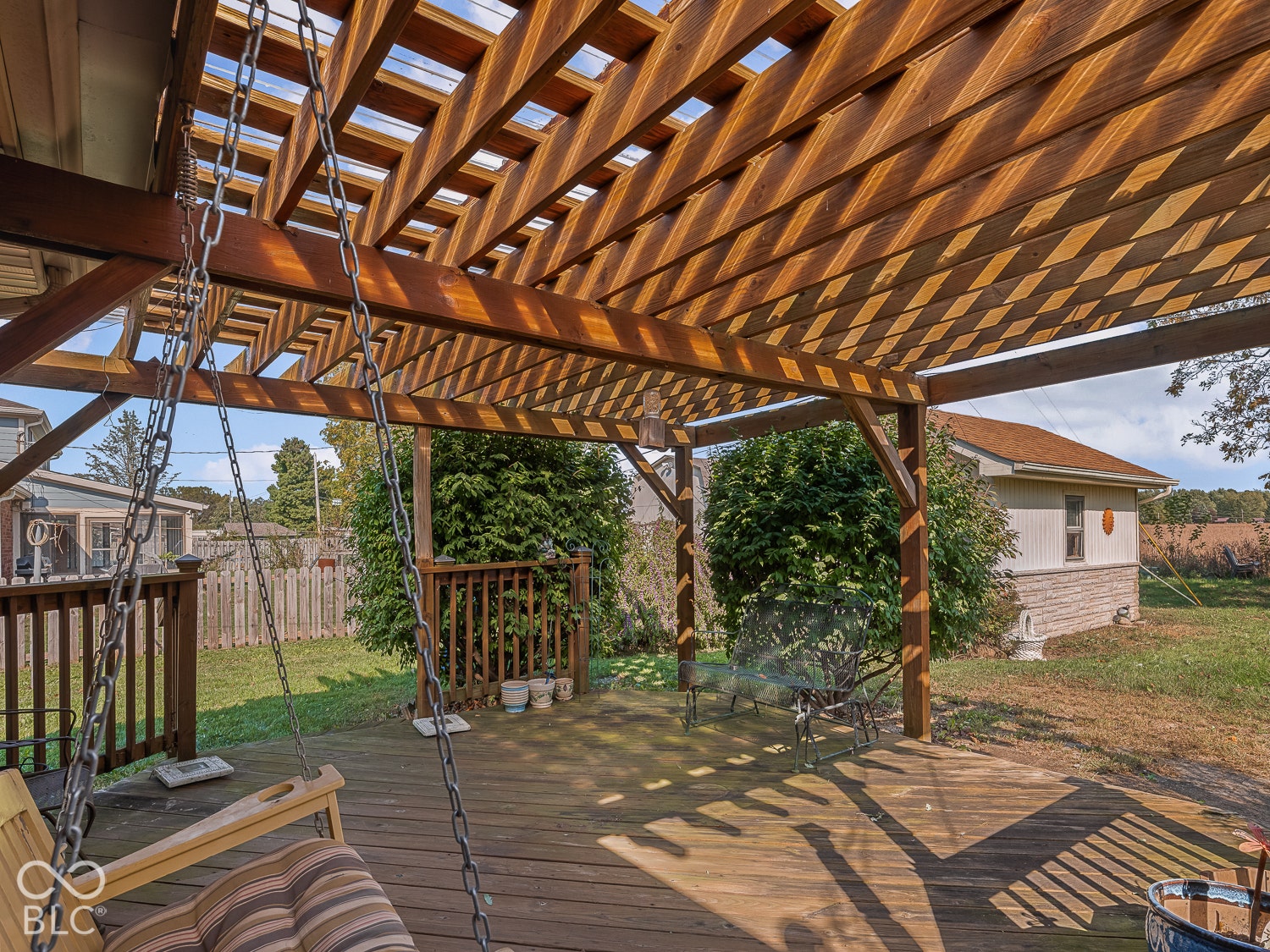 Wood-plank deck featuring a large overhead pergola, wooden railing, and a chain-suspended swing
