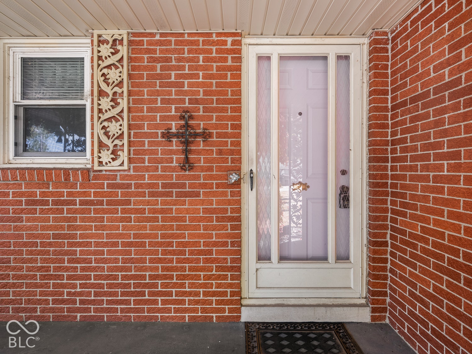 Red brick exterior featuring a porch with a front entry storm door, decorative vertical masonry detailing, and a double-hung window