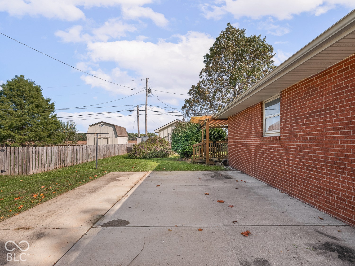 Red brick exterior featuring a concrete parking pad, wood pergola,  with a storage structure