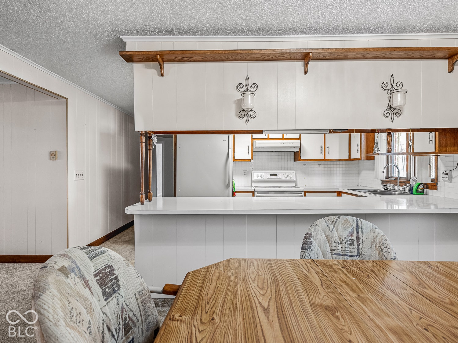 Kitchen featuring a pass-through breakfast bar with countertop, white cabinetry, integrated decorative wall-mounted light fixtures, and wood-finish display shelving