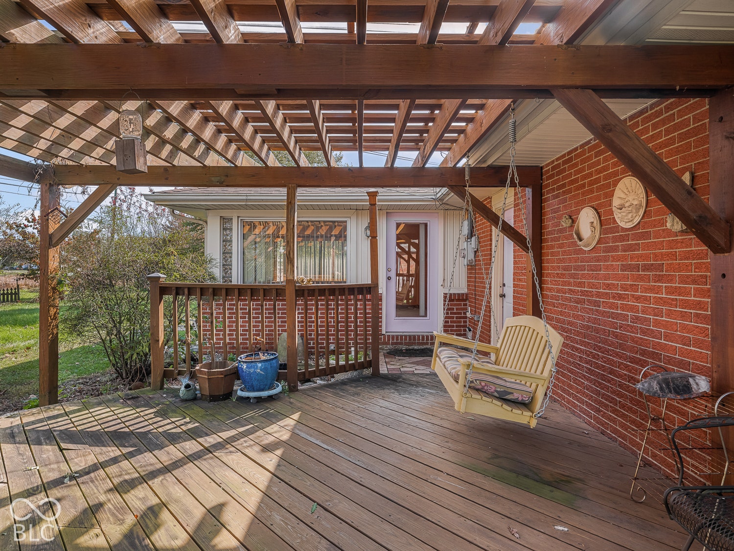 Covered wood deck featuring a timber pergola, brick exterior siding, and a wooden balustrade