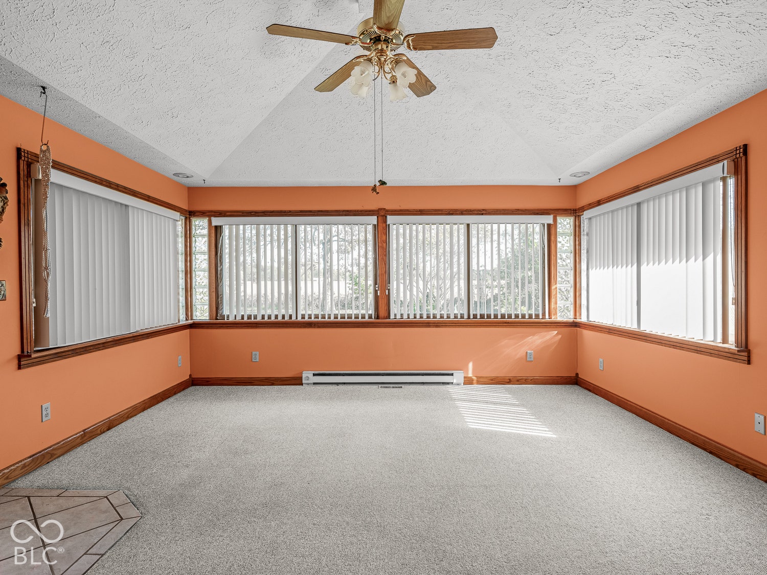 Vaulted ceiling with a central multi-blade ceiling fan, expansive window walls, and wood-trim framing