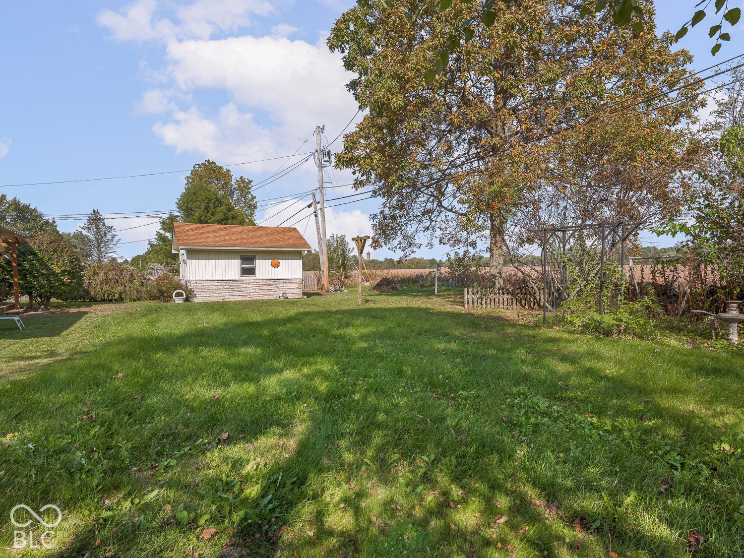 Expansive yard featuring mature trees, a detached storage building with stone-finish masonry, and a metal trellis