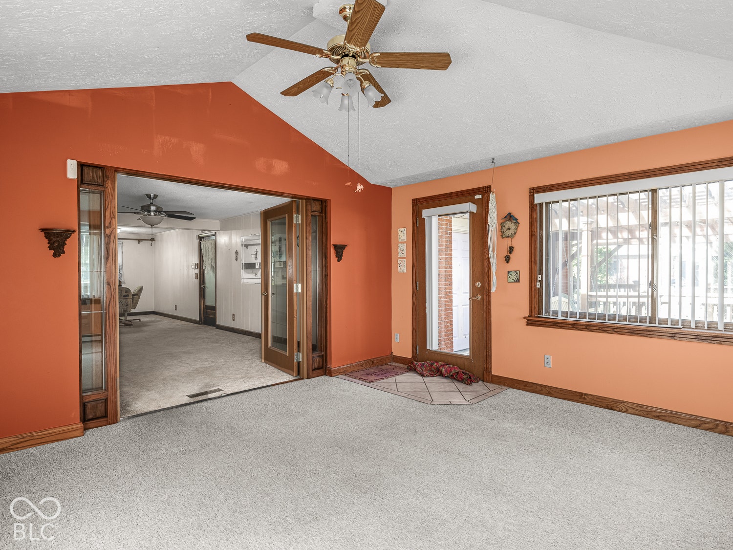 Vaulted ceiling featuring a central wooden ceiling fan with integrated lighting, expansive wooden-framed glass French doors, and a wood-trimmed exterior door with a window insert