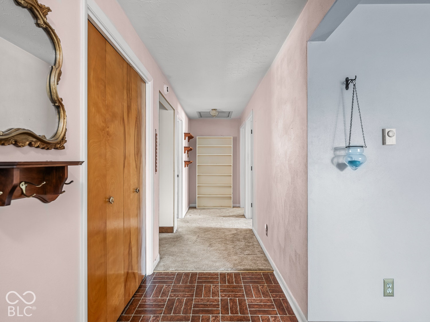 Interior hallway featuring brick-patterned flooring, solid wood-finish bi-fold doors, and a built-in floor-to-ceiling shelving unit