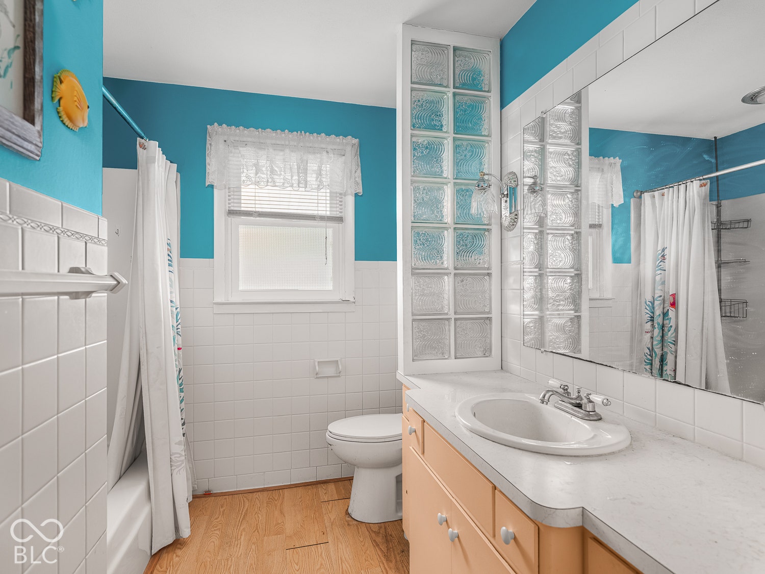 Bathroom featuring a built-in vanity with an integrated basin, glass block privacy screen, wall-to-wall mirror, tiled tub surround, and wood-finish flooring