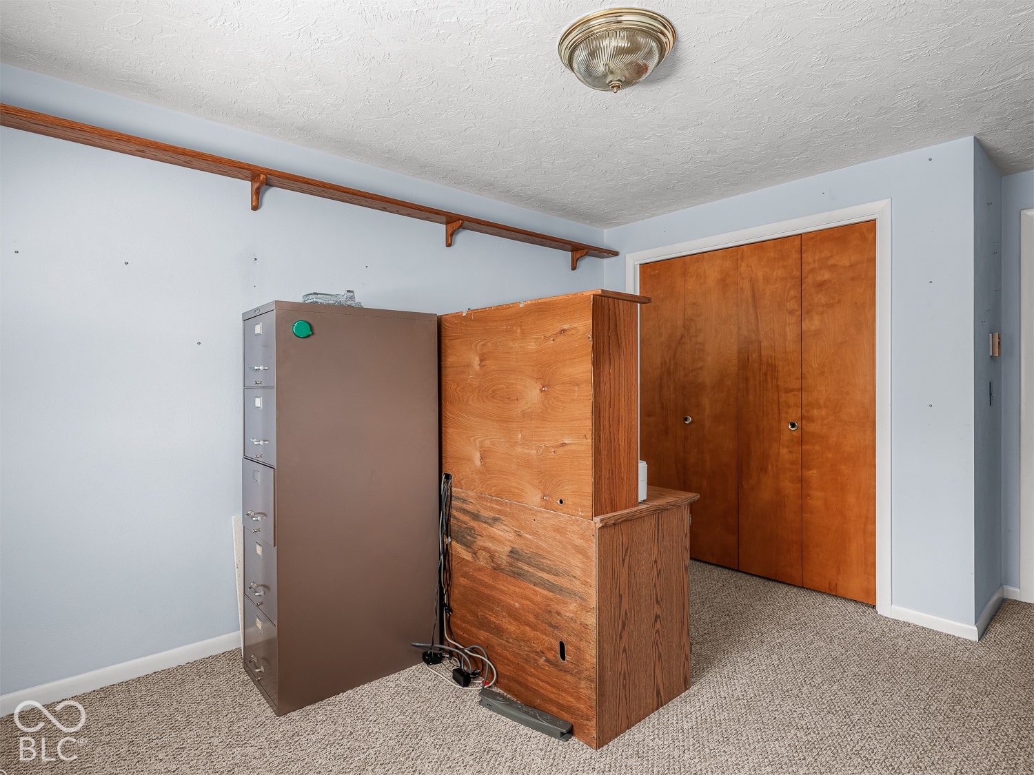 Room featuring wall-to-wall carpeting, dual-door wooden closet, and mounted wooden shelving