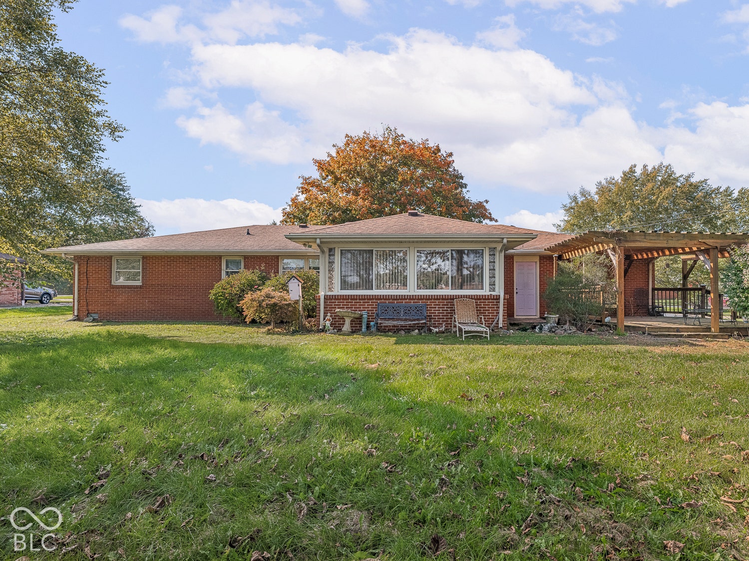 Brick exterior ranch featuring a covered wooden pergola, expansive lawn, and mature trees