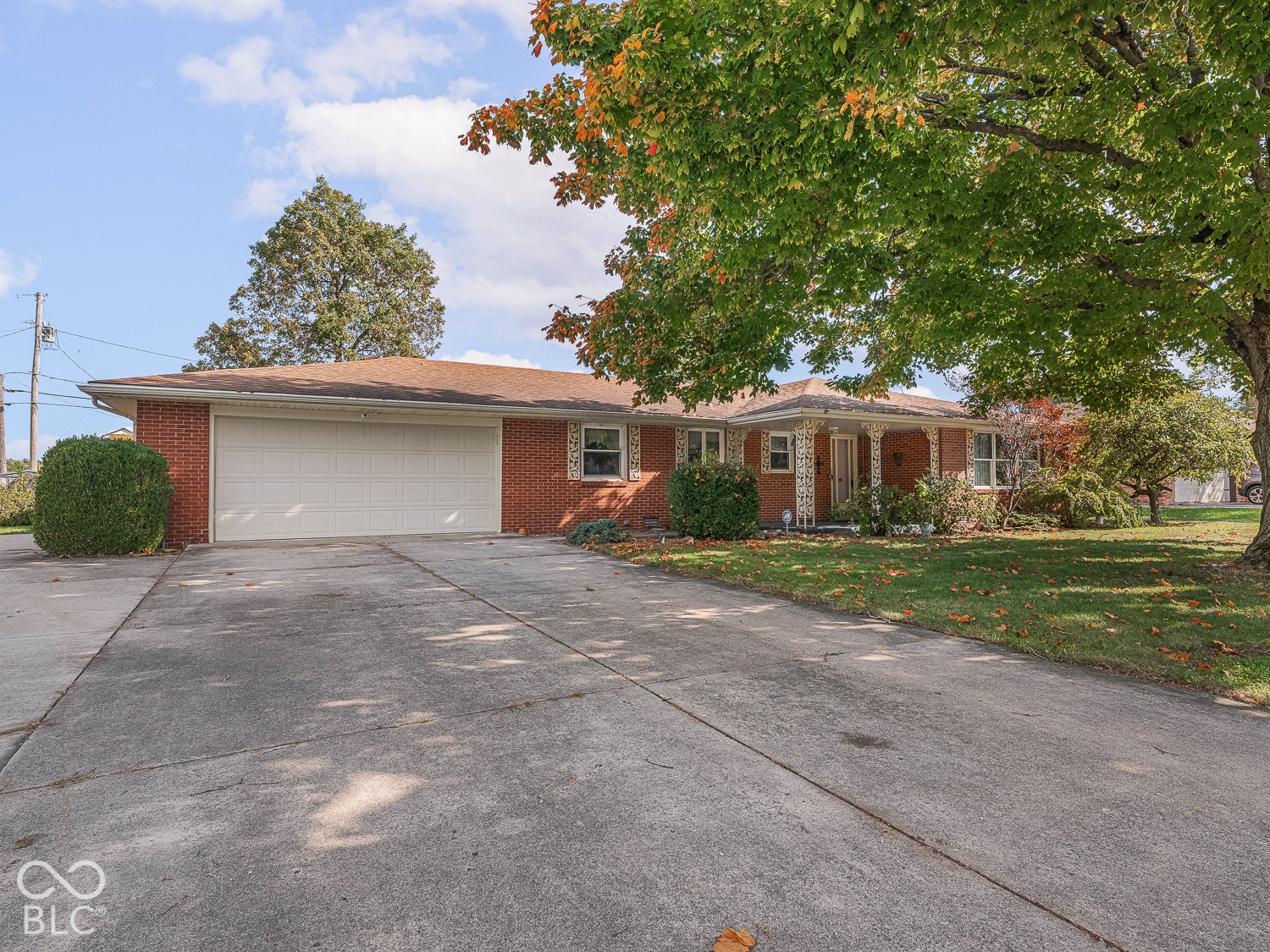 Single-story brick exterior featuring a multi-car attached garage, expanded concrete driveway, and covered front porch with decorative posts