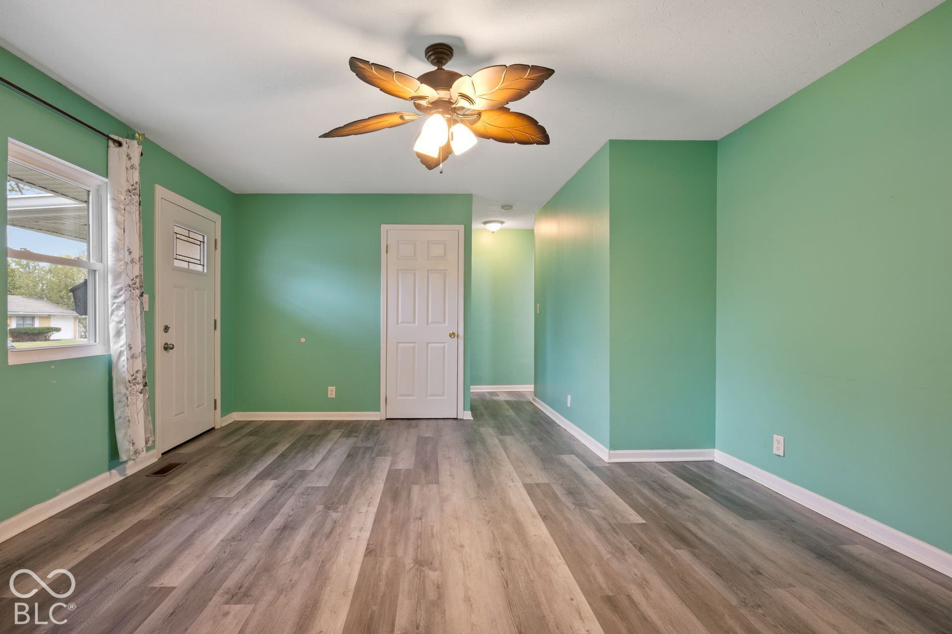 3721 Ireland Drive, Indianapolis, IN 46235 Wood-finish flooring, light-toned wall paint, white-paneled door with inset glass, and a decorative ceiling fan with three glass-shaded lights