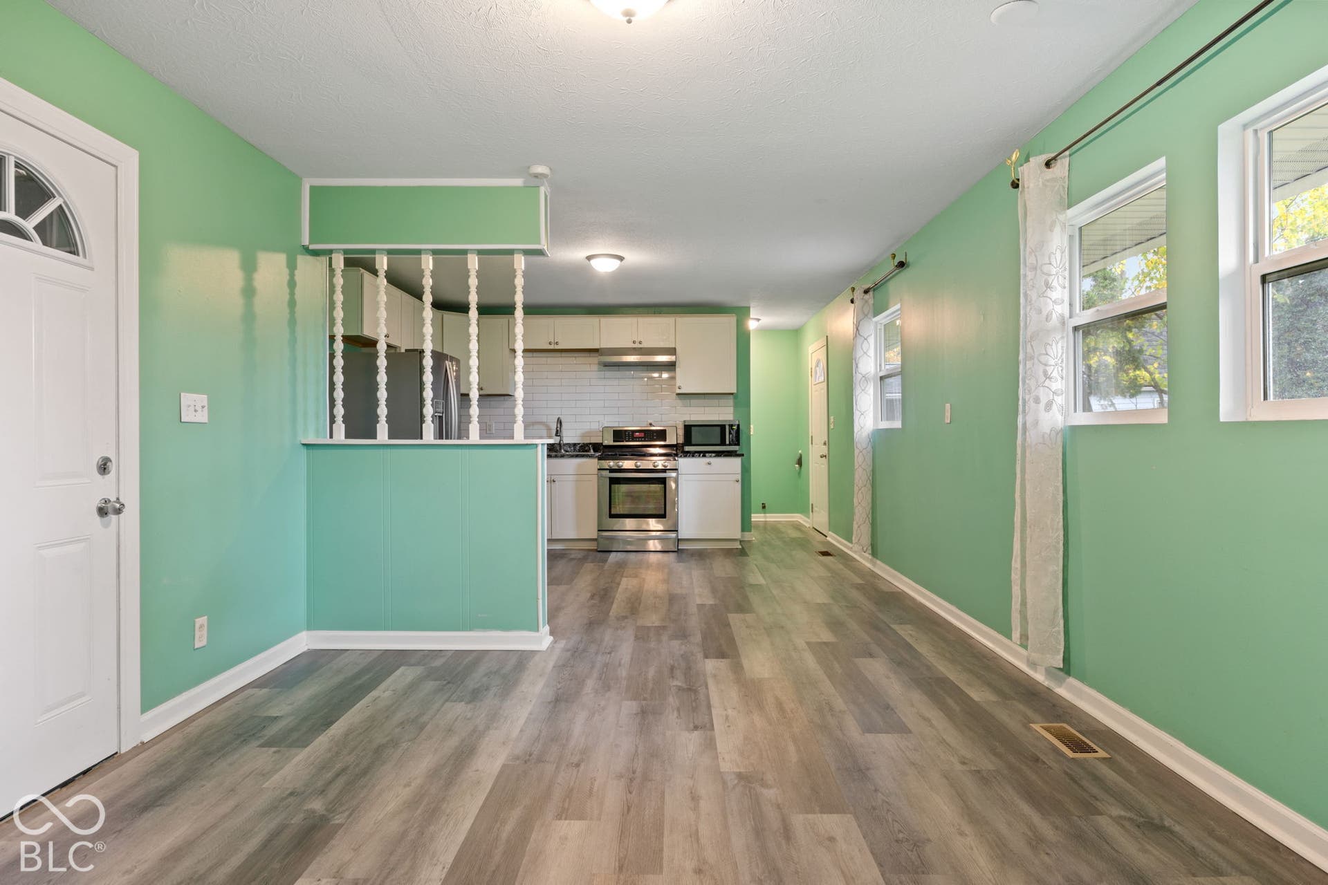 3721 Ireland Drive, Indianapolis, IN 46235 Open-concept interior featuring wood-finish flooring, white cabinetry, stainless steel range, and a decorative spindled partition