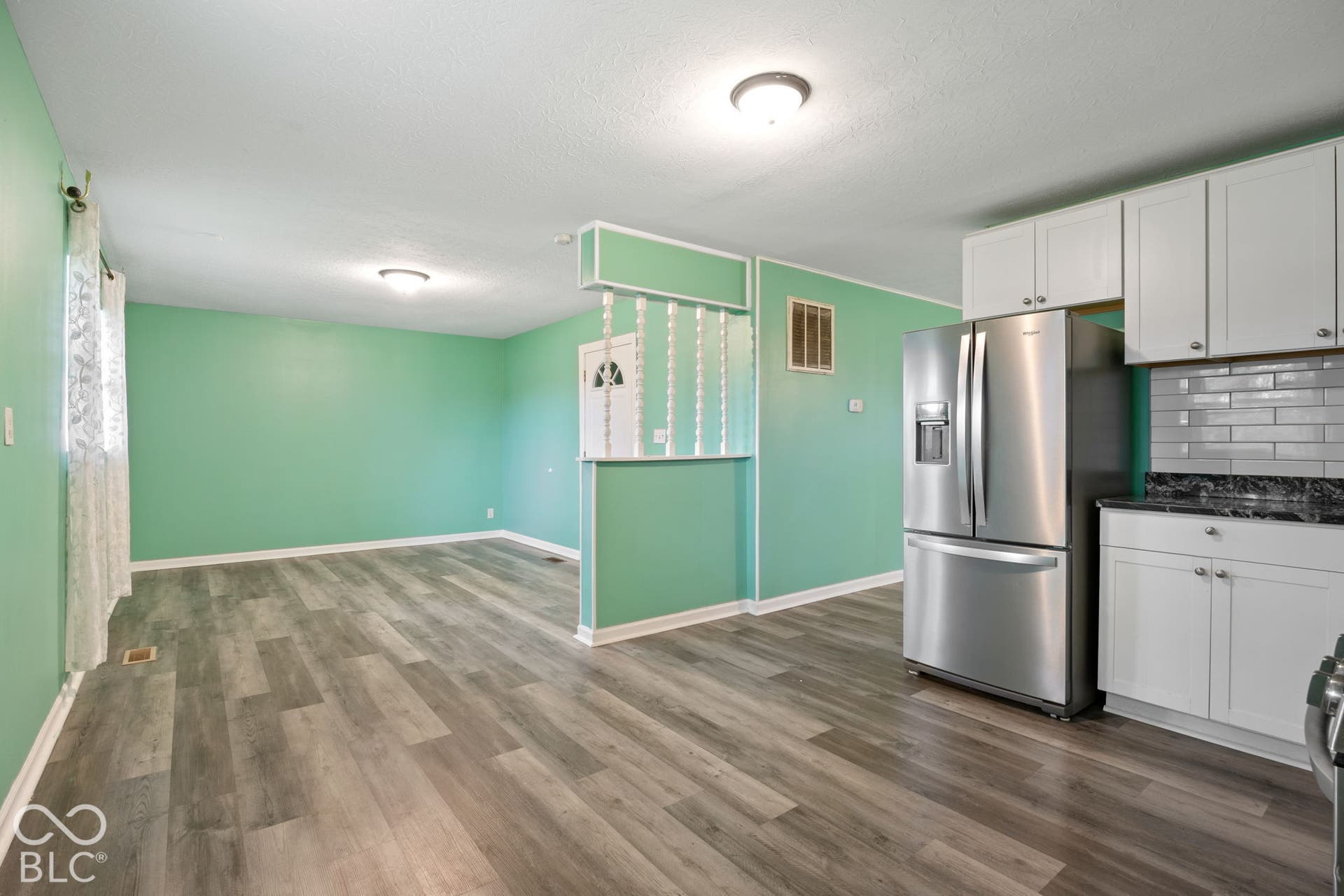 3721 Ireland Drive, Indianapolis, IN 46235 Kitchen featuring white cabinetry, subway tile backsplash, and stainless steel refrigerator, complemented by wood-finish flooring and a decorative spindle partition
