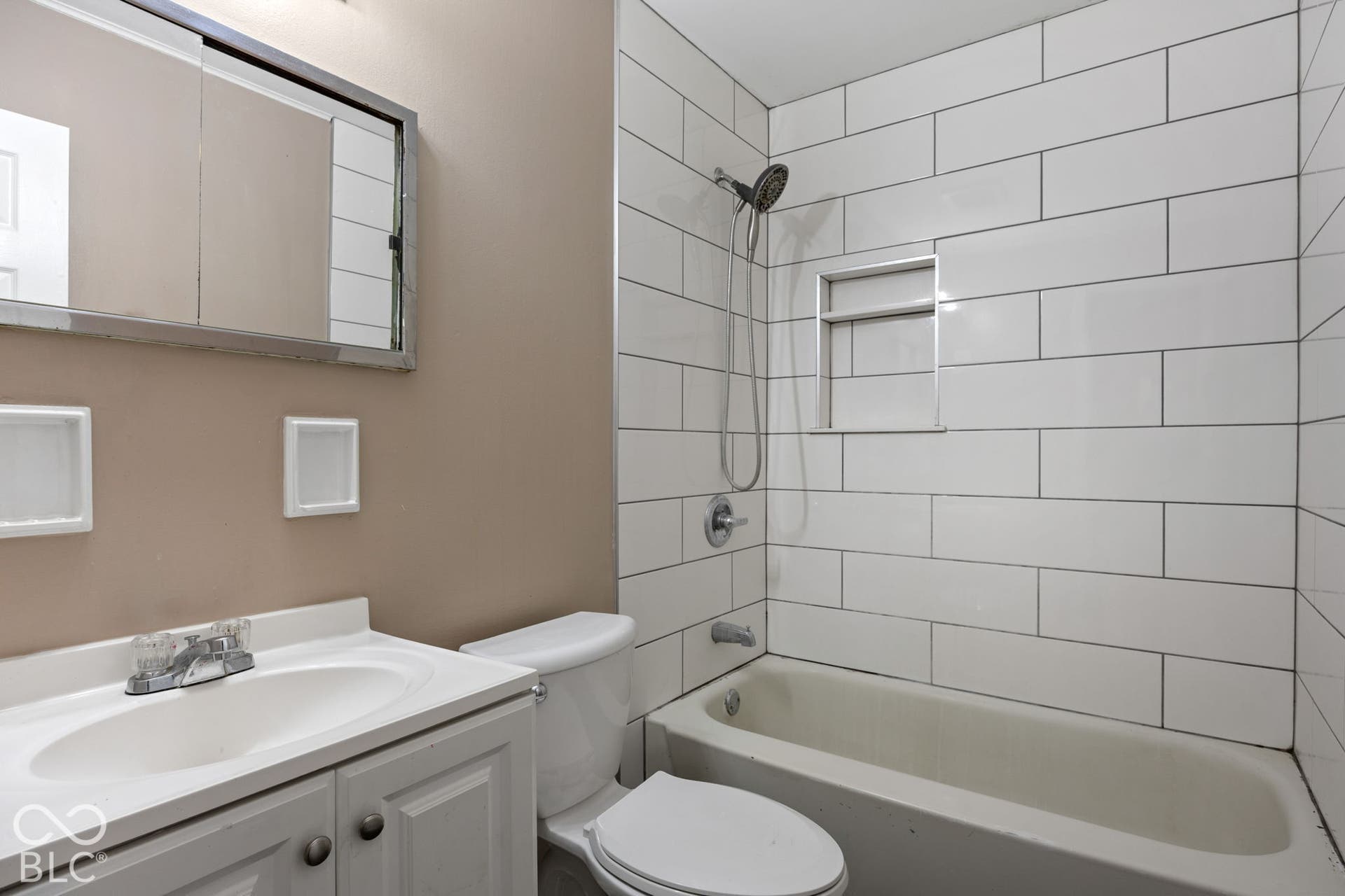 3721 Ireland Drive, Indianapolis, IN 46235 Bathroom featuring a white vanity cabinet with an integrated sink, rectangular wall-mounted mirrored medicine cabinet, and a shower-tub combination with white subway tile surround and a recessed built-in shelving niche