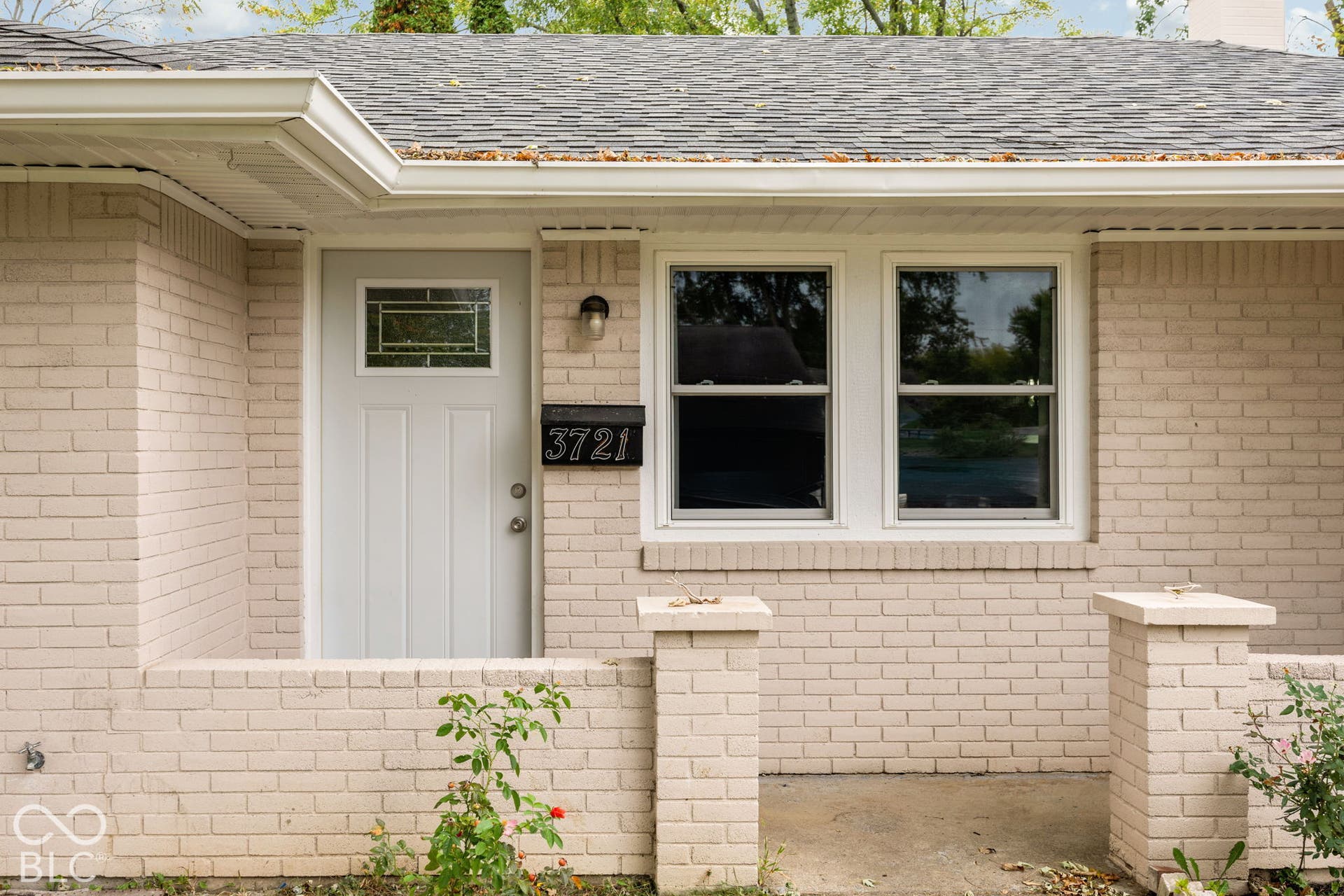 3721 Ireland Drive, Indianapolis, IN 46235 Painted brick exterior featuring a covered porch, low-profile brick retaining wall, single-panel entry door with an integrated window, and dual double-hung windows