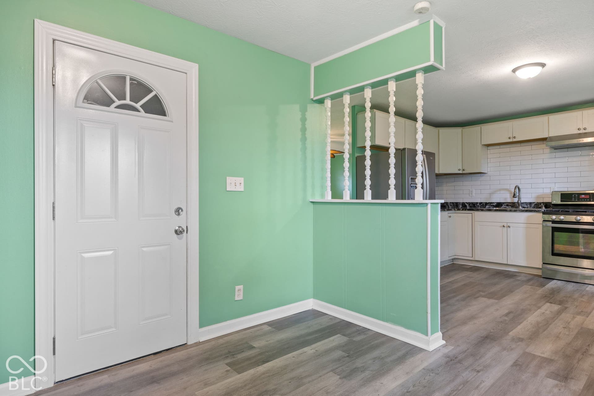 3721 Ireland Drive, Indianapolis, IN 46235 Entryway featuring a semi-private room divider with decorative spindles, wood-finish flooring, white cabinetry, a subway tile backsplash, and stainless steel kitchen appliances