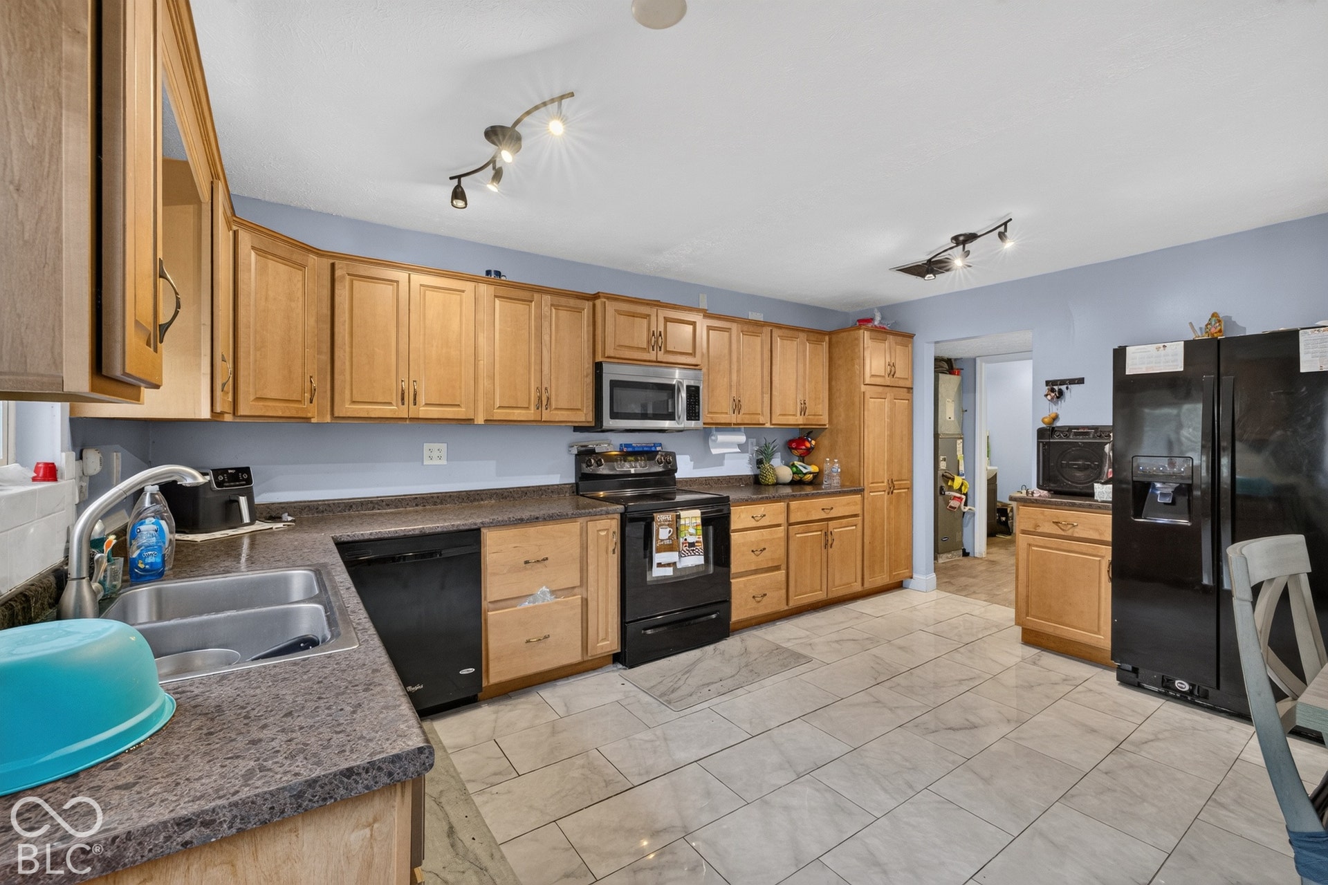 Kitchen featuring natural wood cabinetry, stone-finish countertops, tile flooring, integrated black appliances, and multi-directional track lighting