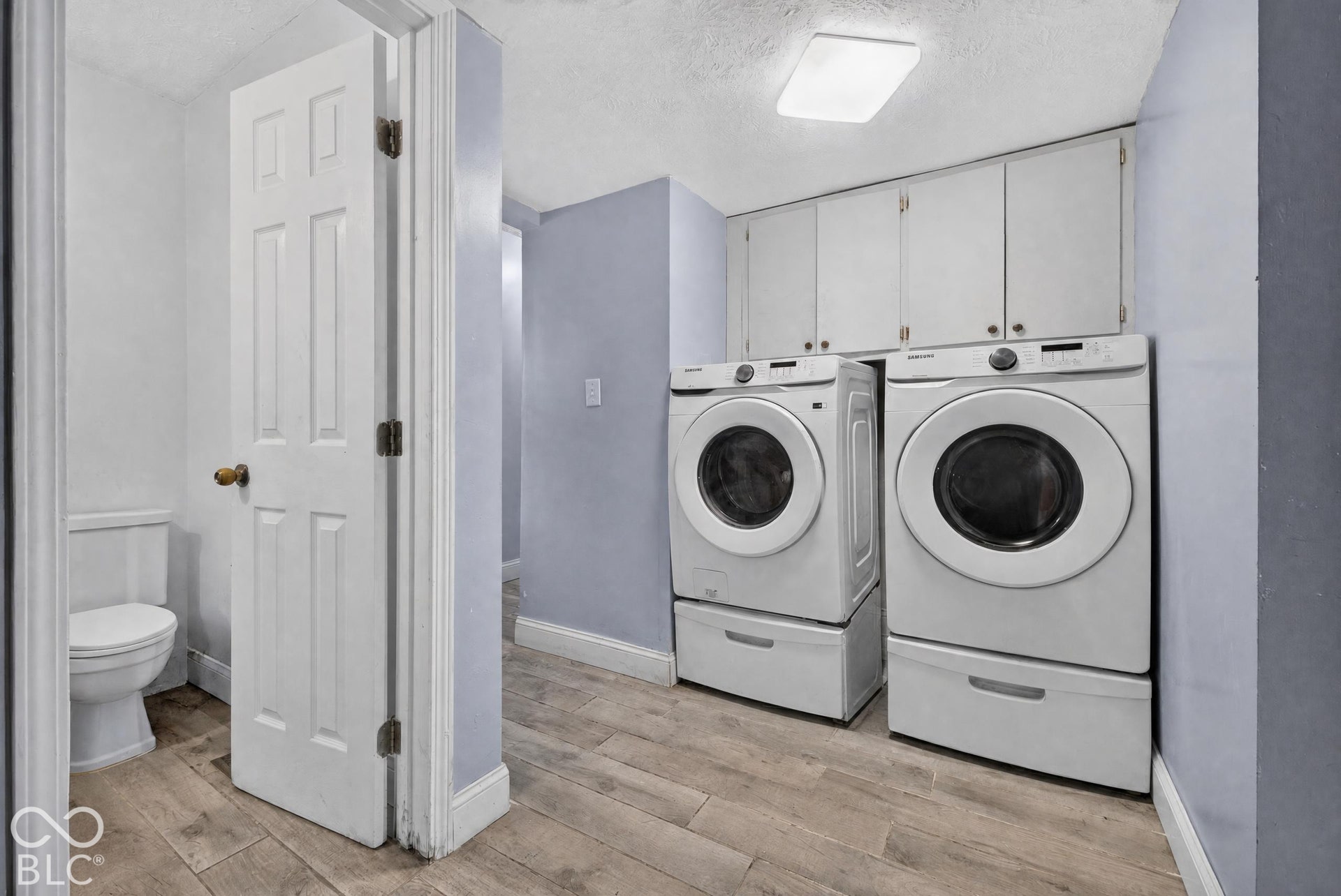 Laundry area featuring wood-finish flooring, ceiling-mounted lighting, and overhead built-in cabinetry