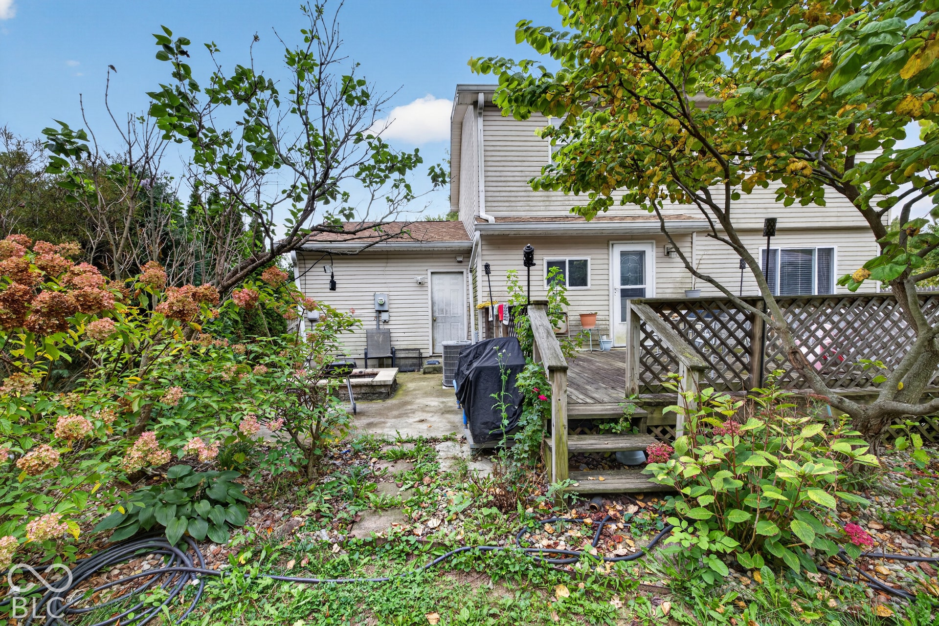 Rear exterior featuring a raised wood deck with lattice railing, stone-surfaced patio, and mature landscaping