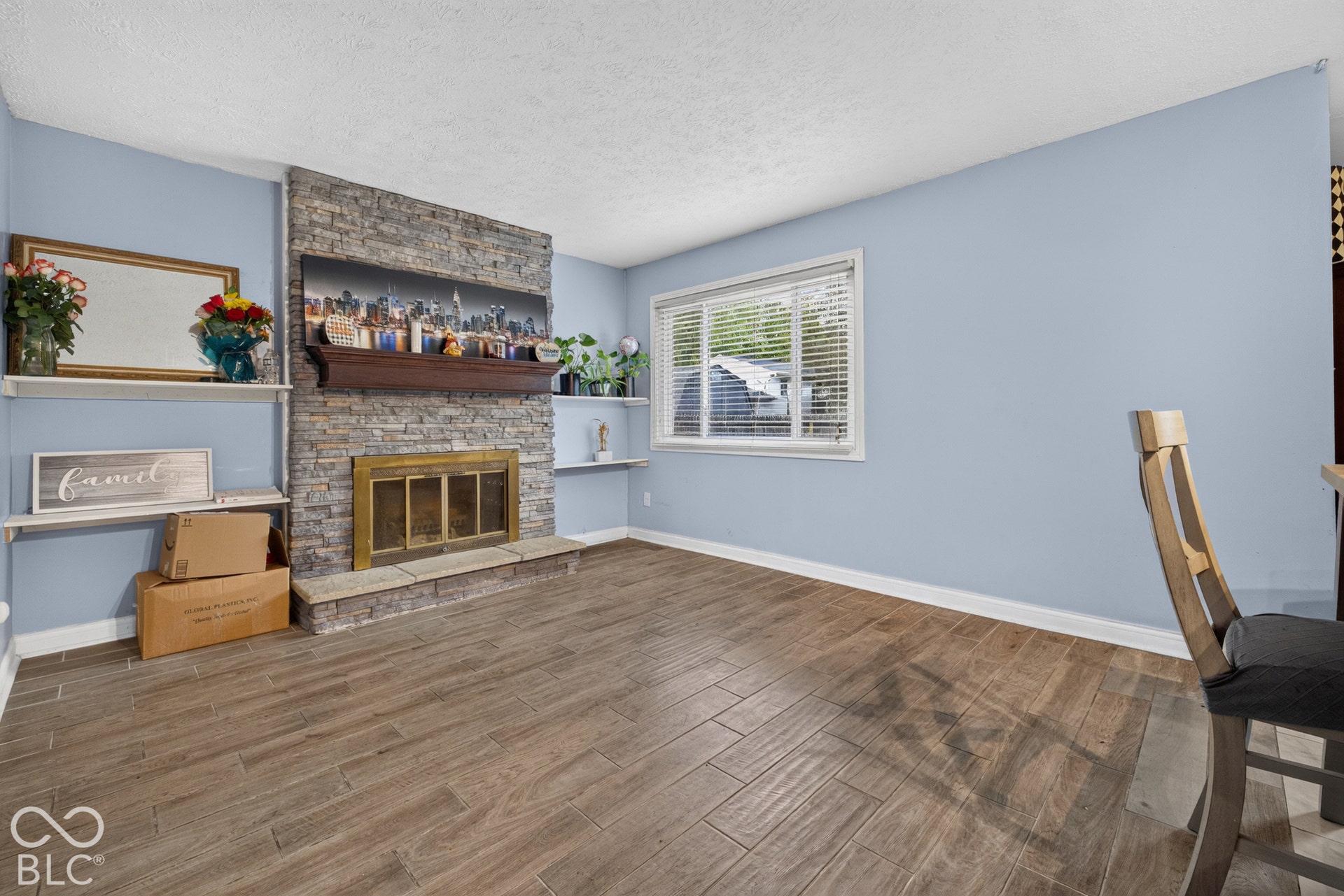 Living area featuring wood-finish tile flooring, a floor-to-ceiling stone fireplace, a raised stone hearth, a prominent wood mantel, and built-in shelving