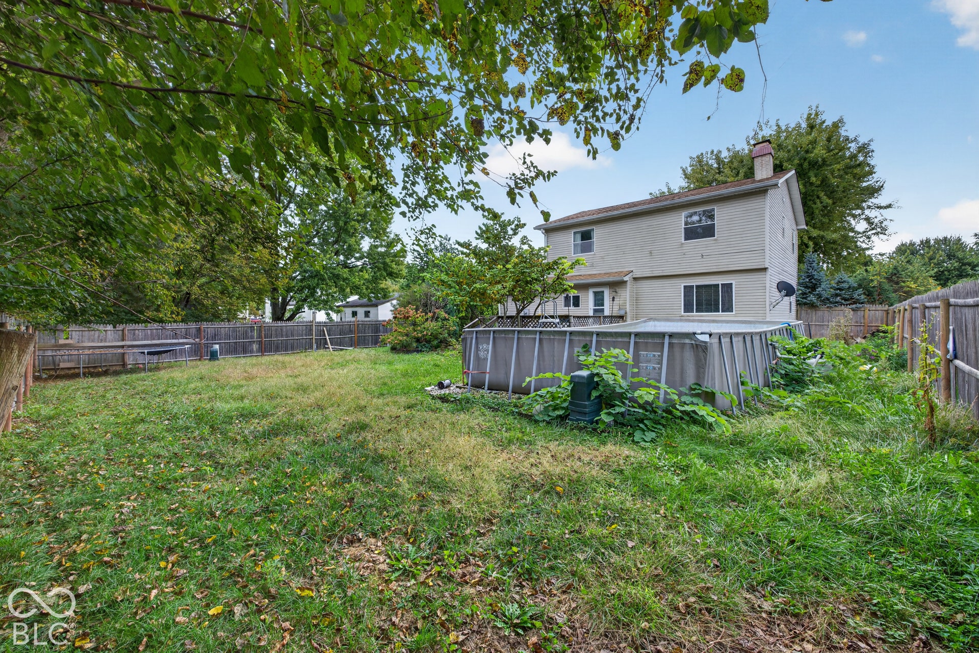 Two-story residence featuring brick siding, a chimney, wood-style fencing, and a grassy backyard