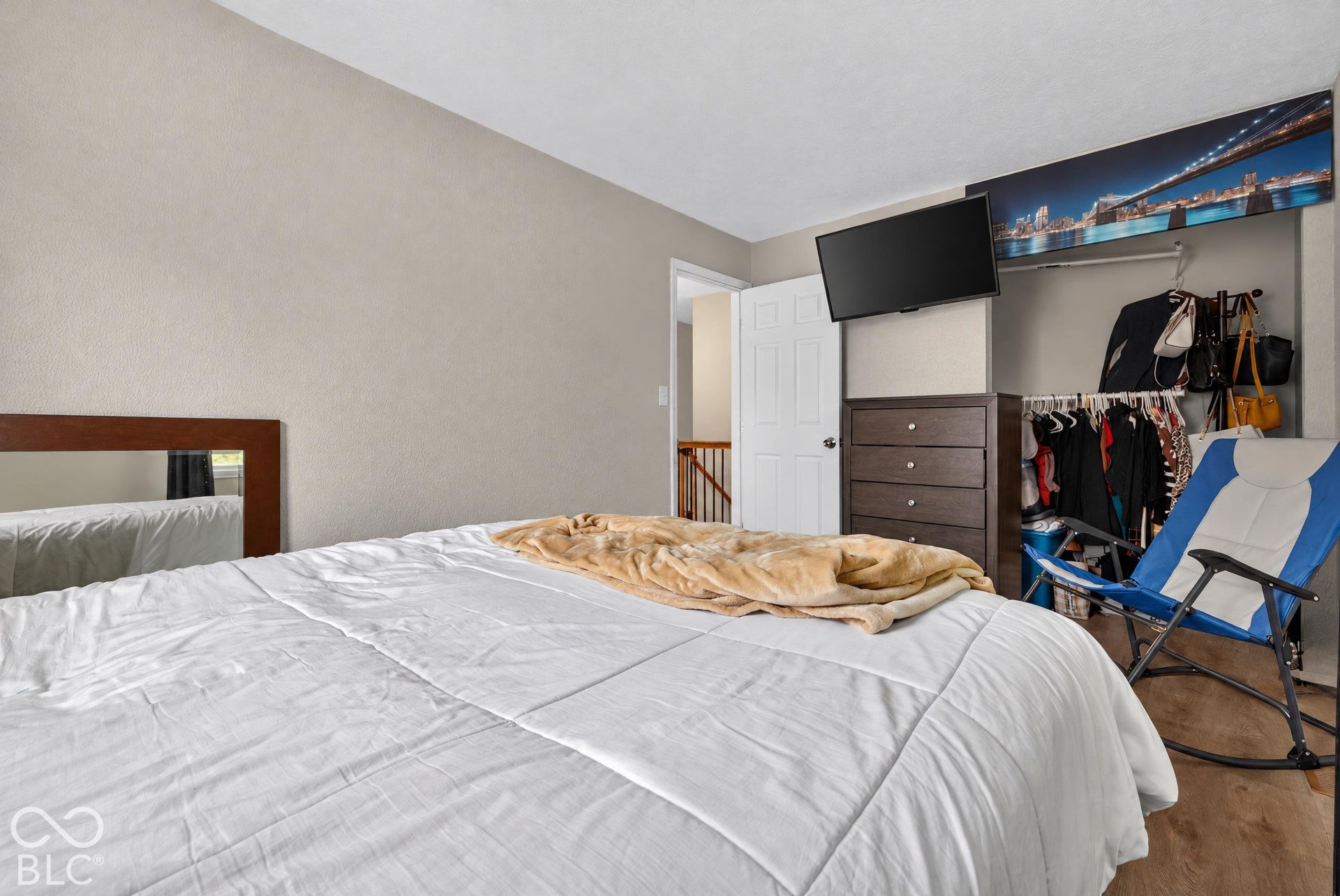 Neutral-toned walls, wood-finish flooring, and an open closet featuring a built-in hanging rod