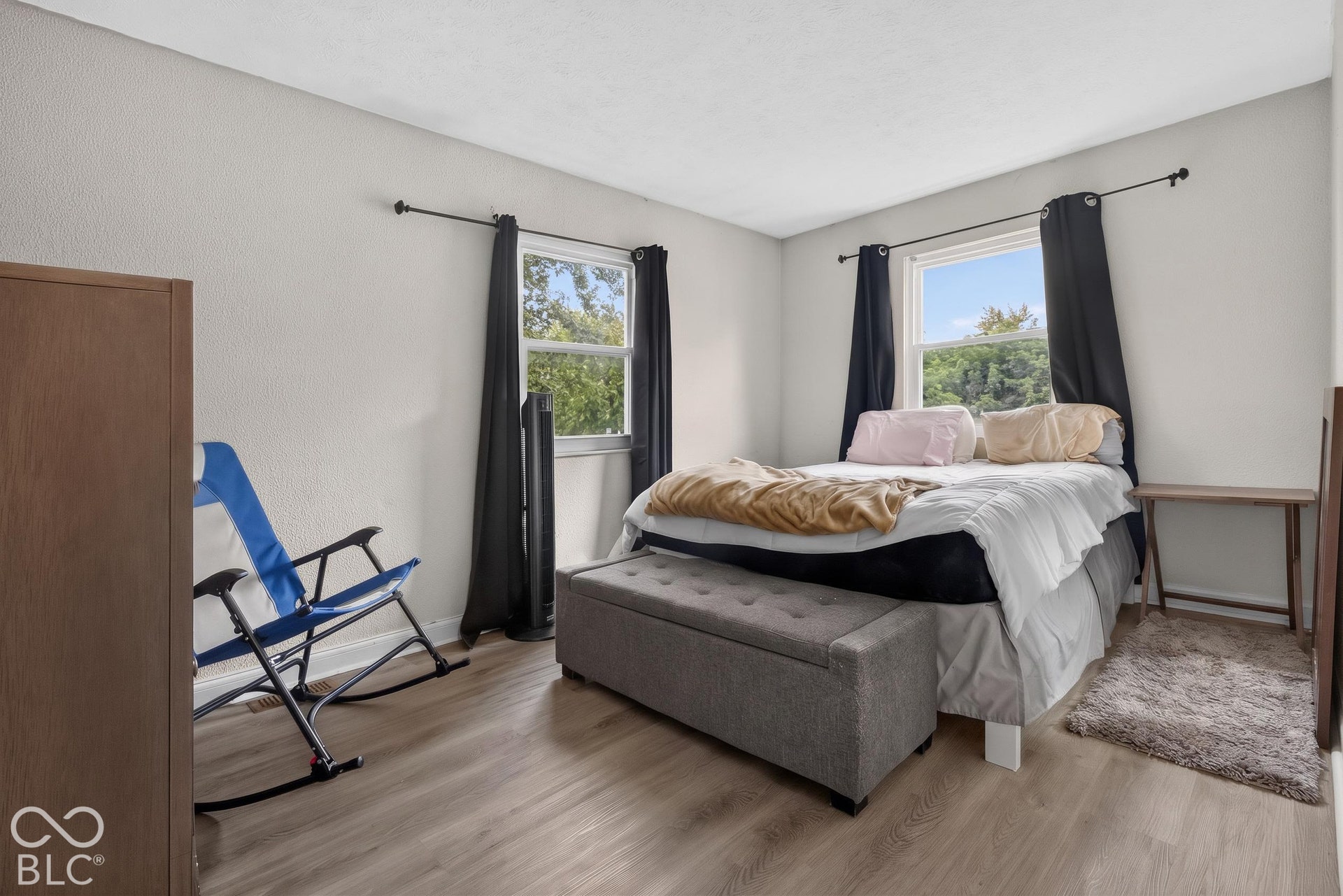 Bedroom featuring neutral wall paint, wood-finish flooring, and two windows with black rod hardware