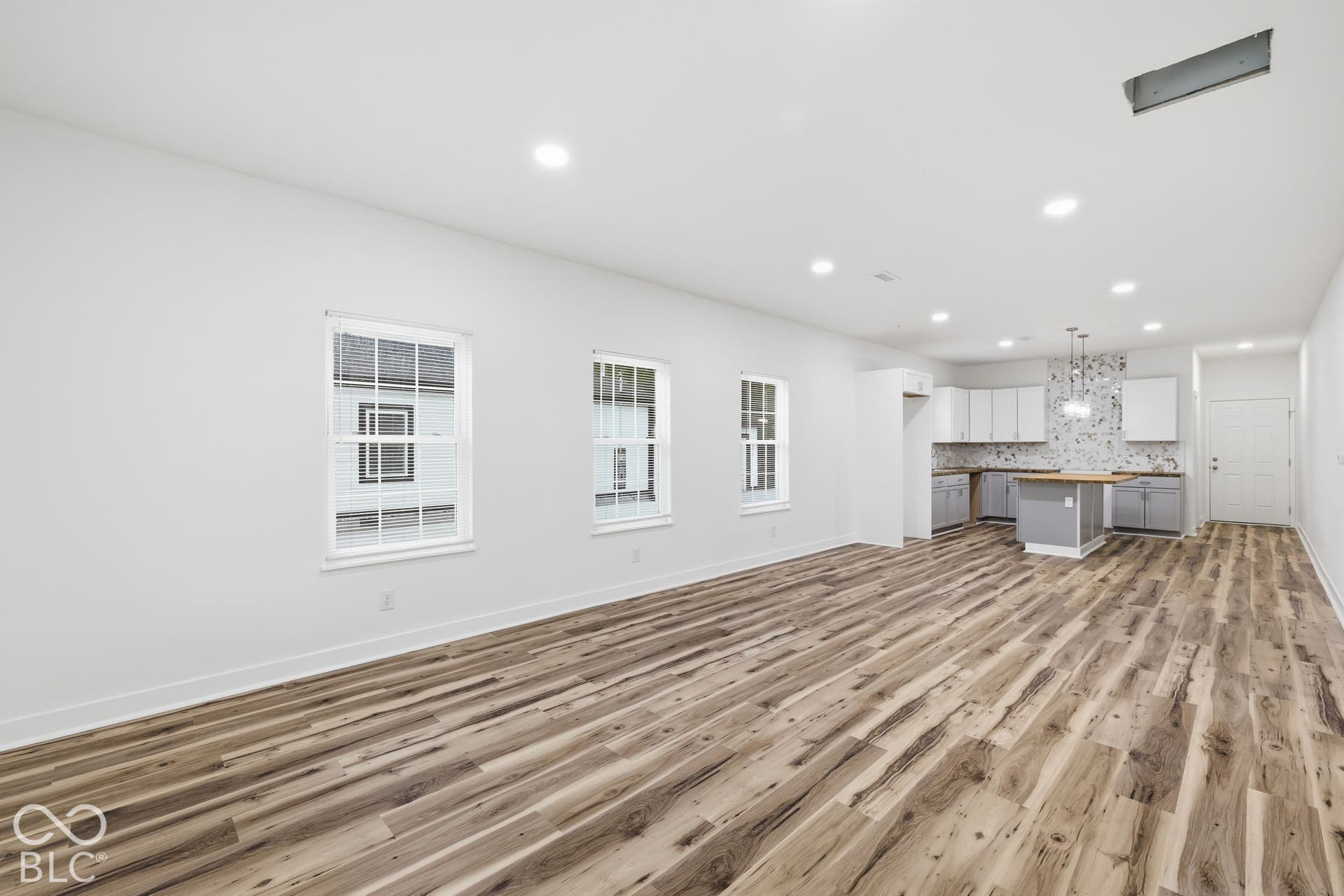 Open-concept interior featuring wood-finish flooring, recessed lighting, multi-pane windows, shaker-style cabinetry, and a central island with a wood countertop