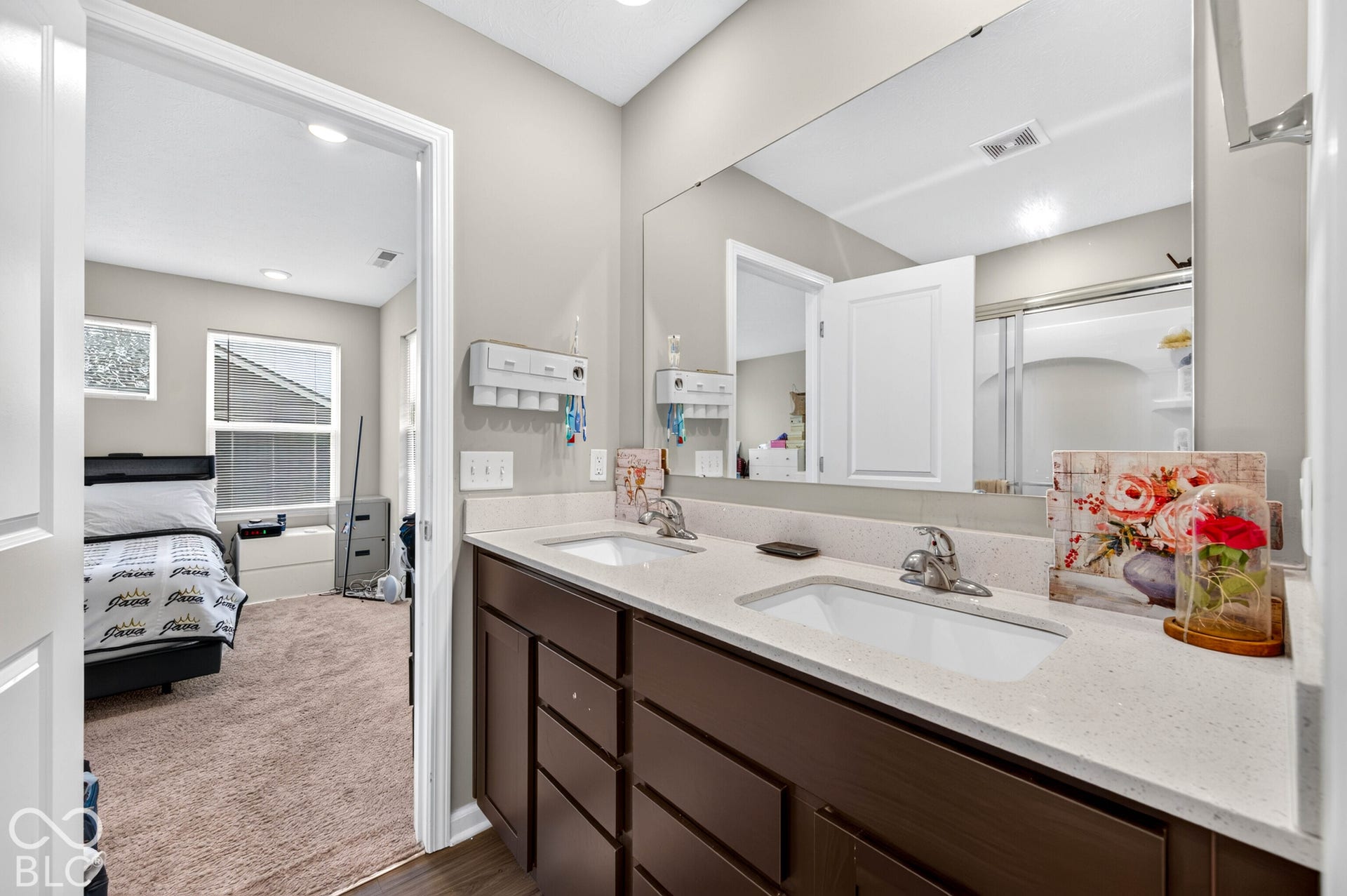 Double vanity with a light-toned solid surface countertop, dual undermount sinks, chrome fixtures, and dark-finish cabinetry featuring a full-width wall mirror