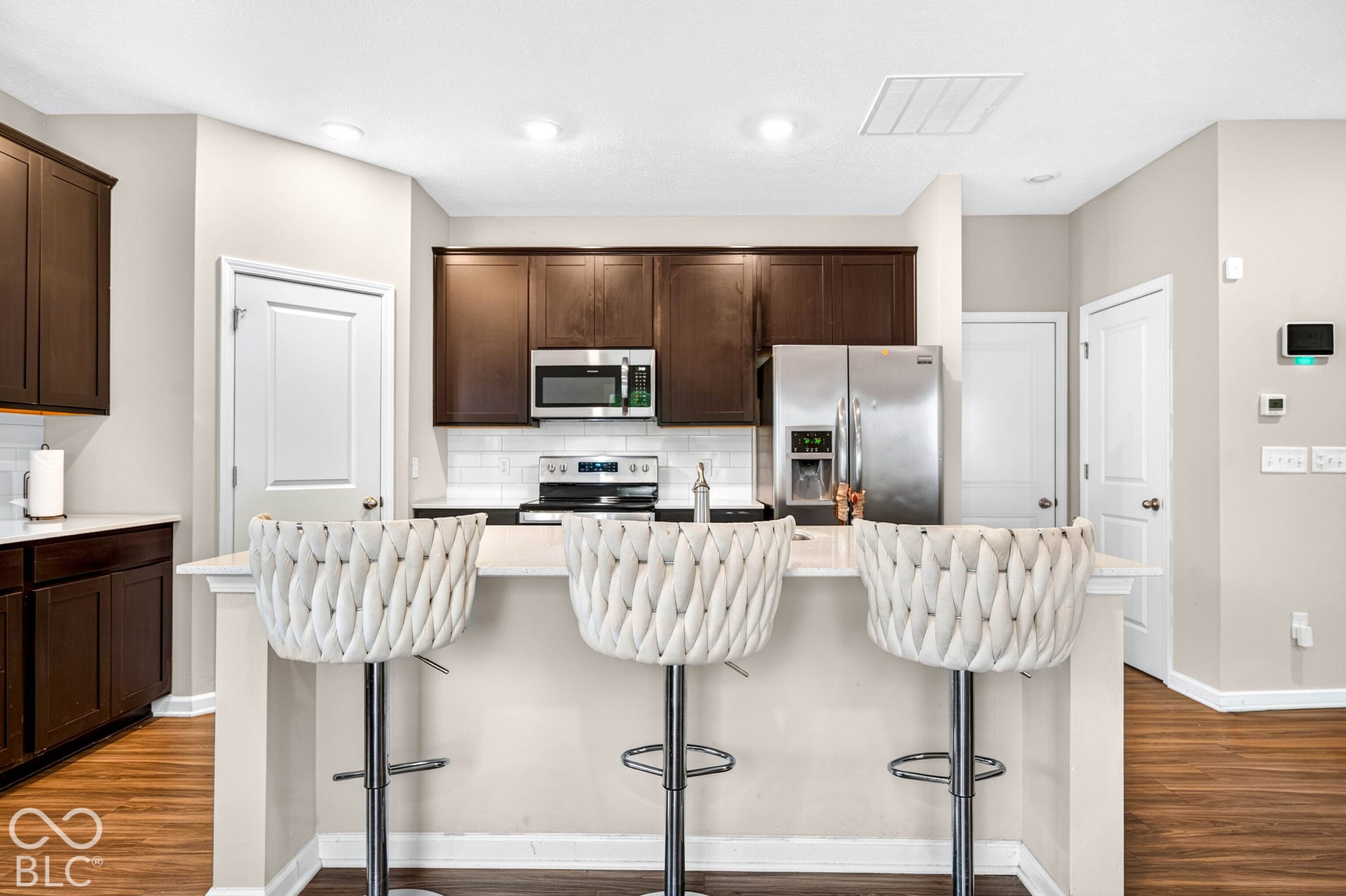 Kitchen featuring dark cabinetry, stone-finish countertops, stainless steel appliances, a tile backsplash, and wood-finish flooring