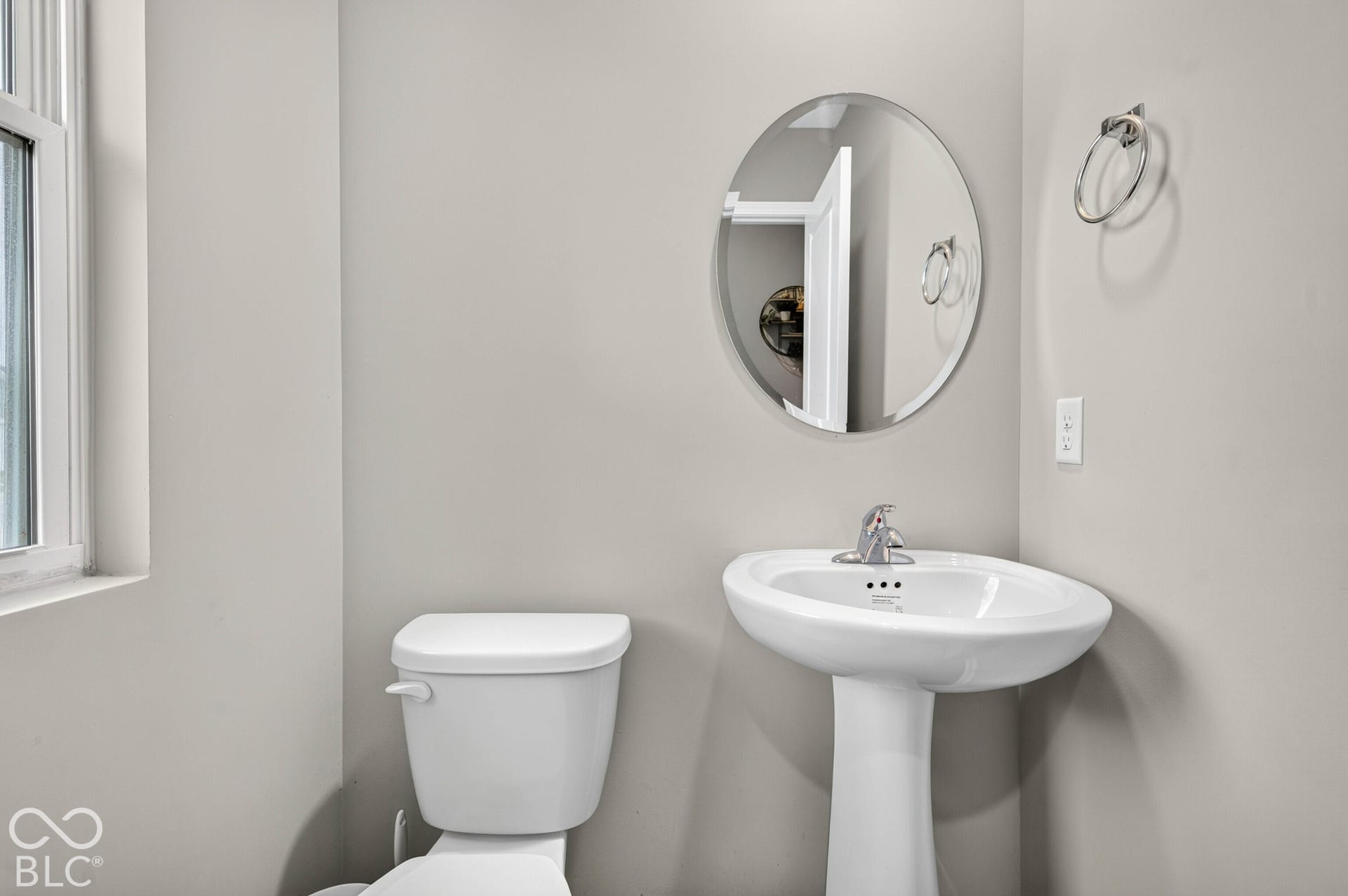 White porcelain pedestal sink with polished chrome faucet, round wall-mounted mirror, and wall-mounted metal towel ring
