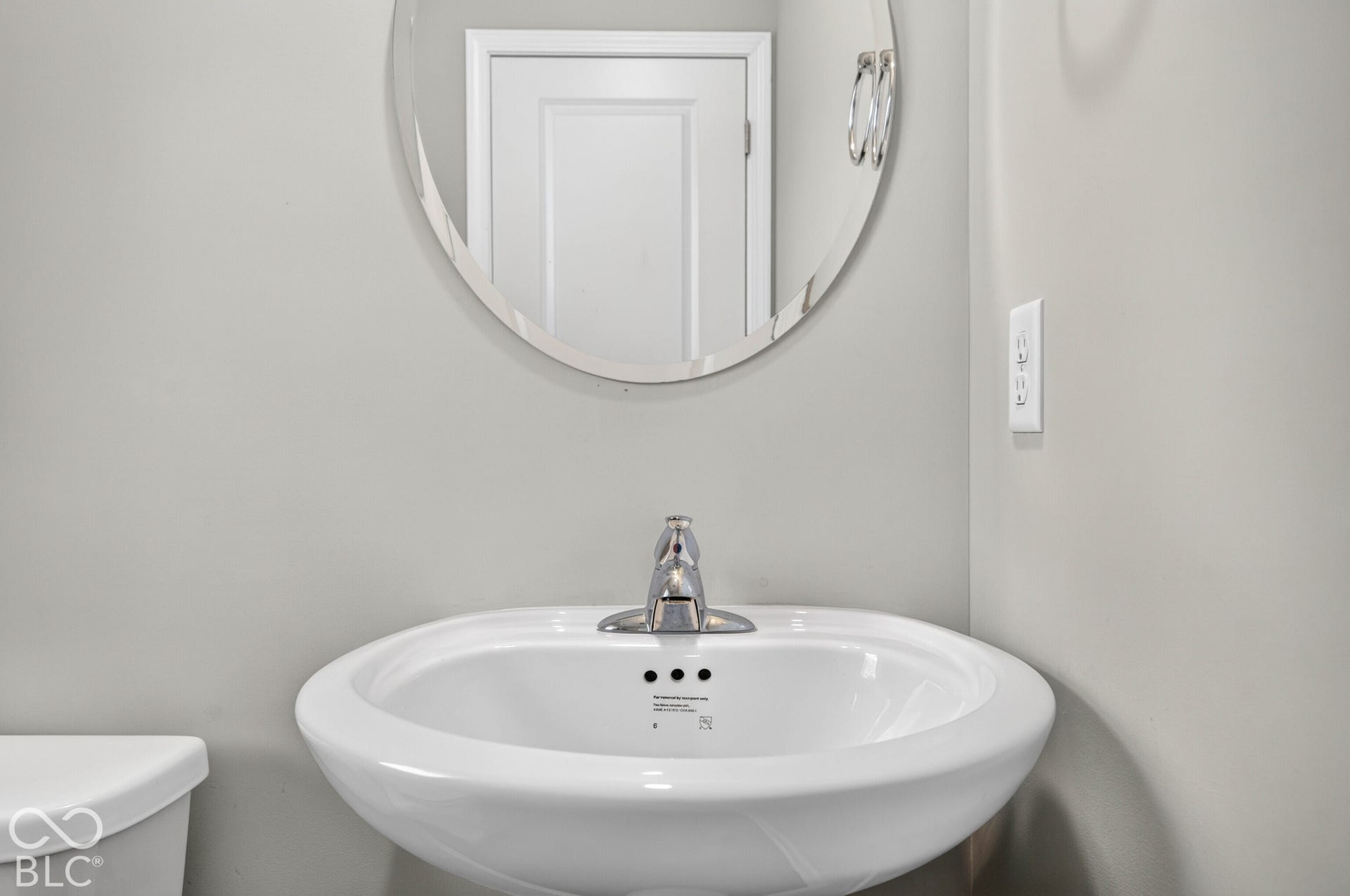 Wall-mounted circular mirror with a polished finish, paired with a white pedestal sink featuring a chrome faucet