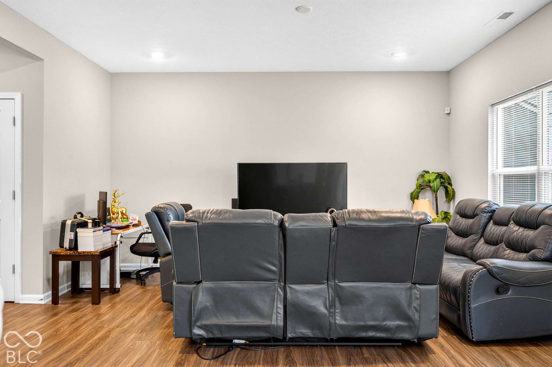 Neutral-toned interior space featuring wood-finish flooring, recessed lighting, and a large window with horizontal blinds