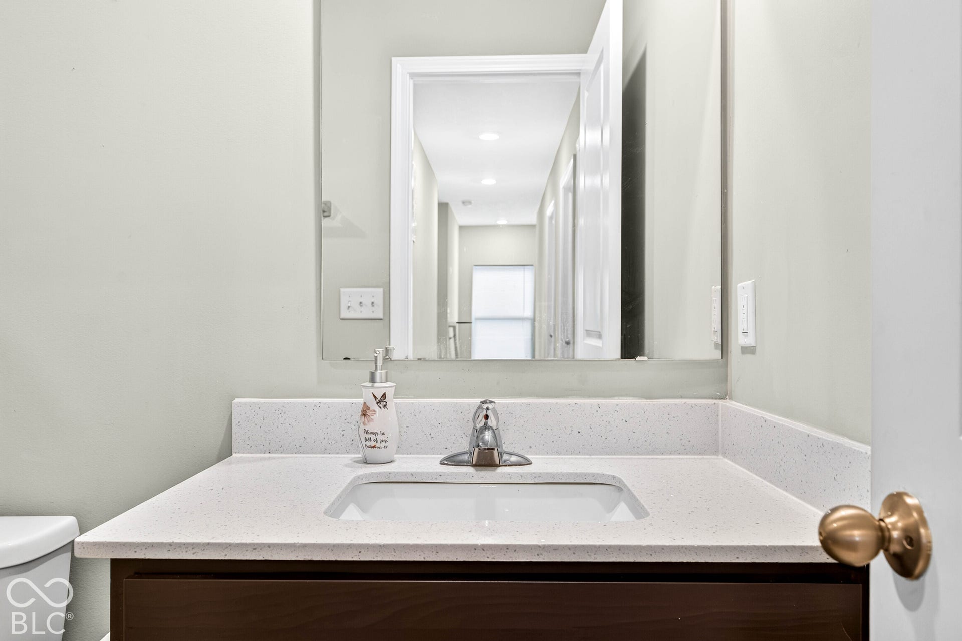 Vanity featuring a dark-finish base cabinet, solid surface countertop with integrated backsplash, and an undermount sink with a center-set polished chrome faucet, paired with a large wall-mounted rectangular mirror
