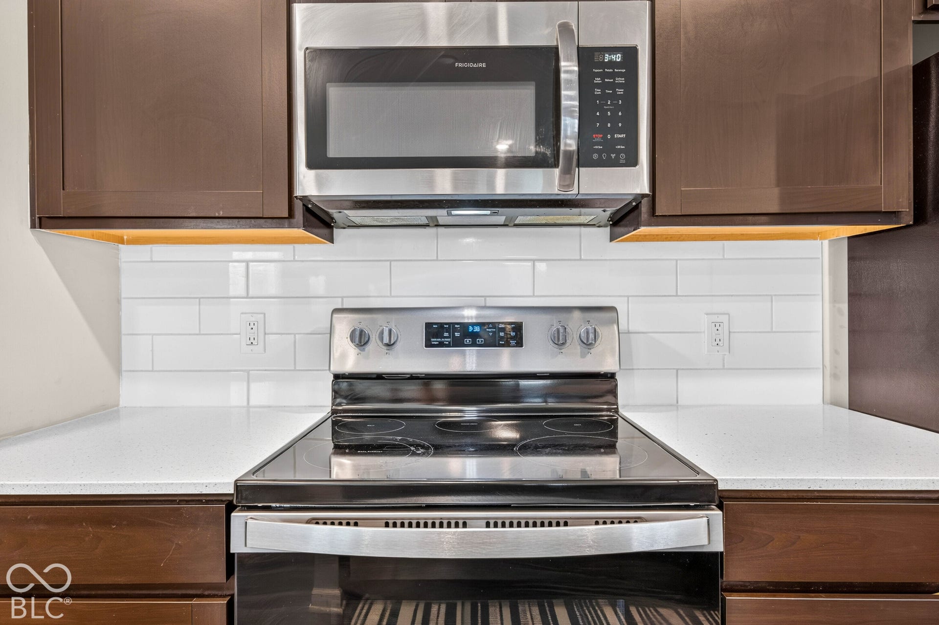 Kitchen featuring dark wood cabinetry, white subway tile backsplash, solid-surface countertops, and stainless steel appliances including an electric range and built-in microwave