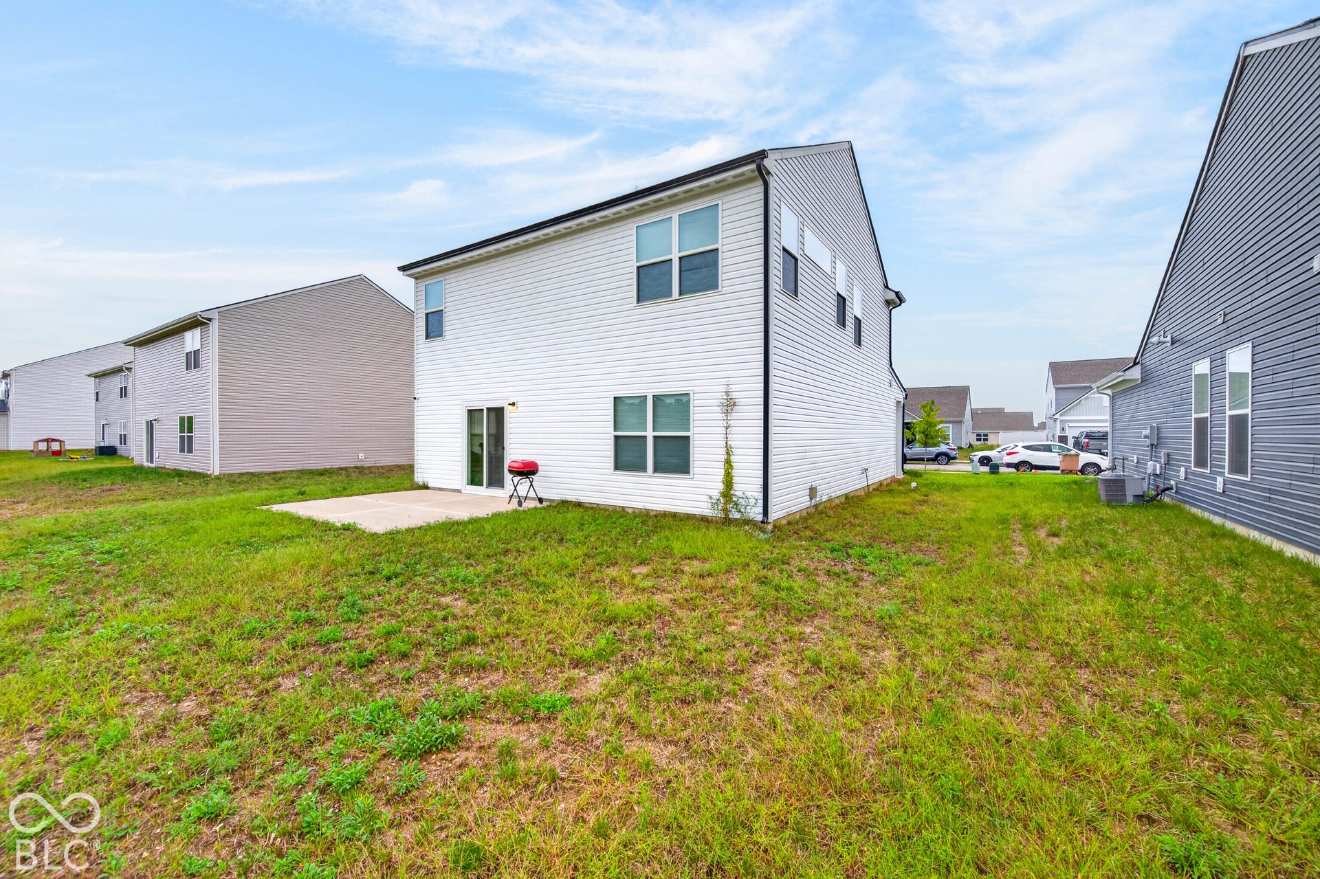 Rear exterior featuring light-colored horizontal siding, a concrete patio, and a grass-covered lot