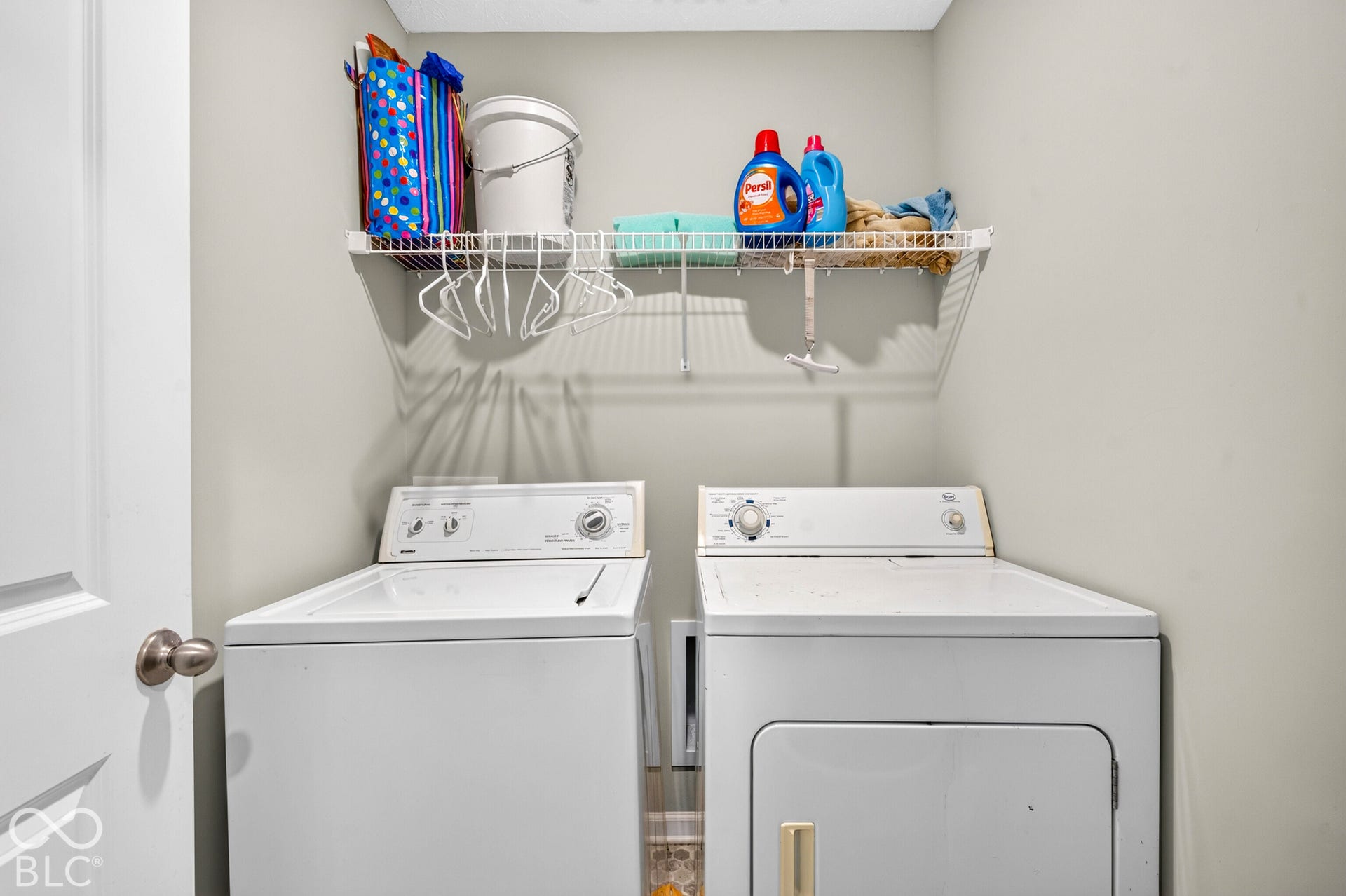 Laundry area featuring white top-load appliances and a wall-mounted wire storage shelf
