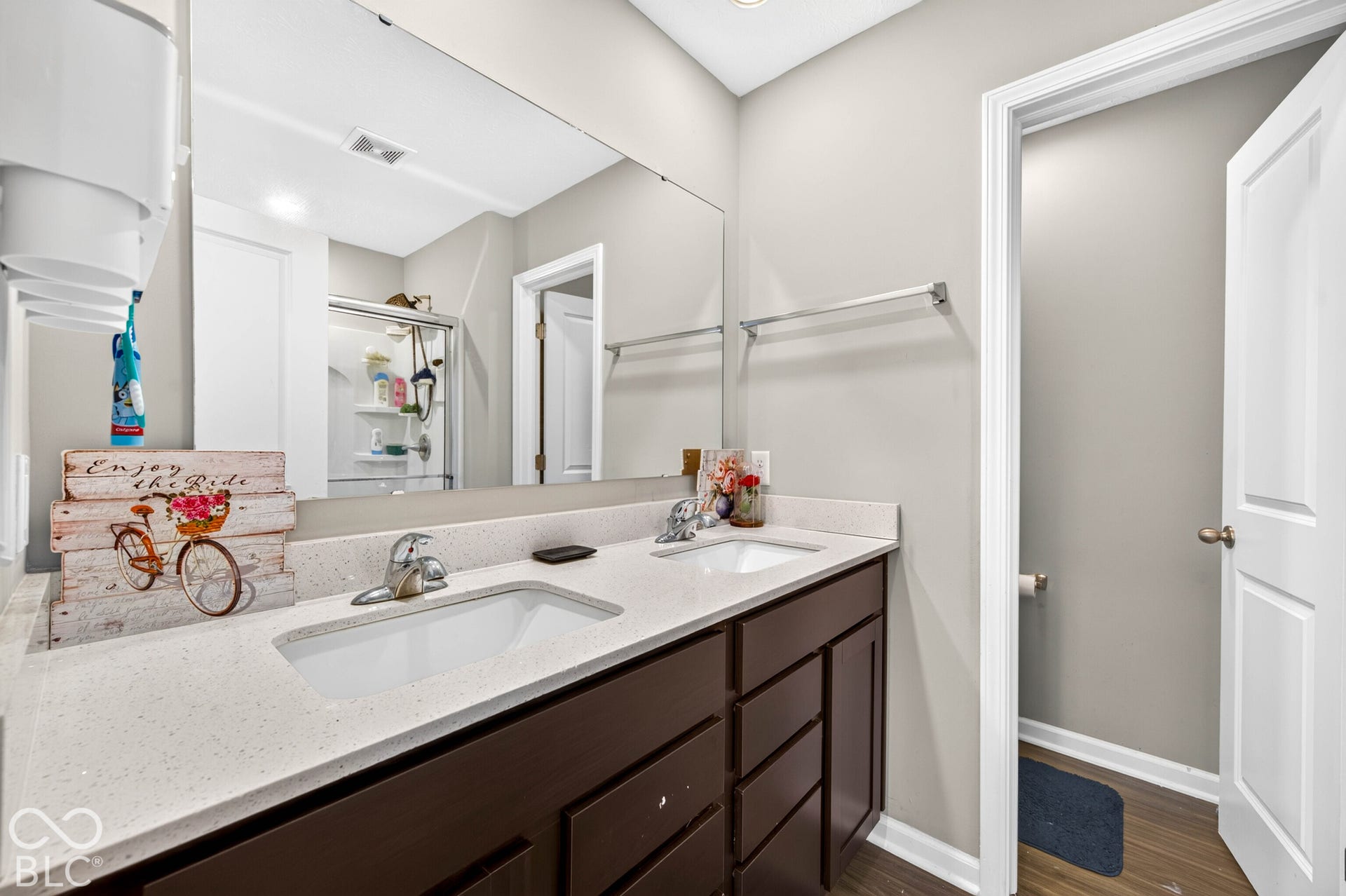 Dual-sink vanity with a solid-surface countertop, dark-finish cabinetry, a full-width wall mirror, and chrome-finish faucets