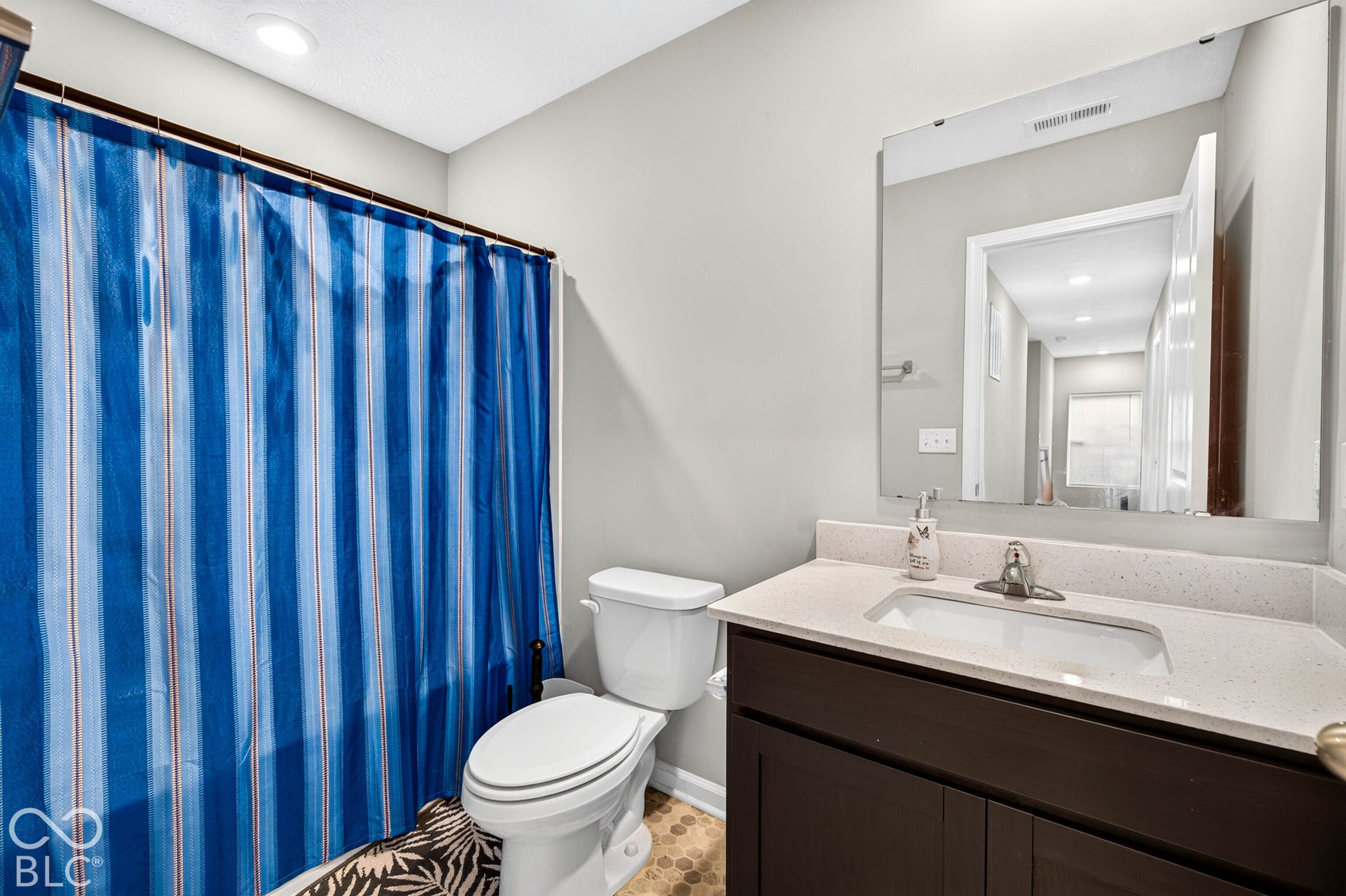 Bathroom featuring a dark wood-finish vanity, light-toned composite countertop with integrated sink, polished chrome faucet, and a large frameless wall-mounted mirror