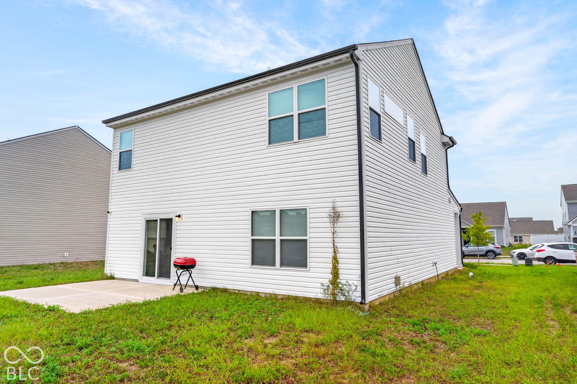 Two-story exterior featuring light-colored horizontal siding, a rear concrete patio, and a sliding glass door