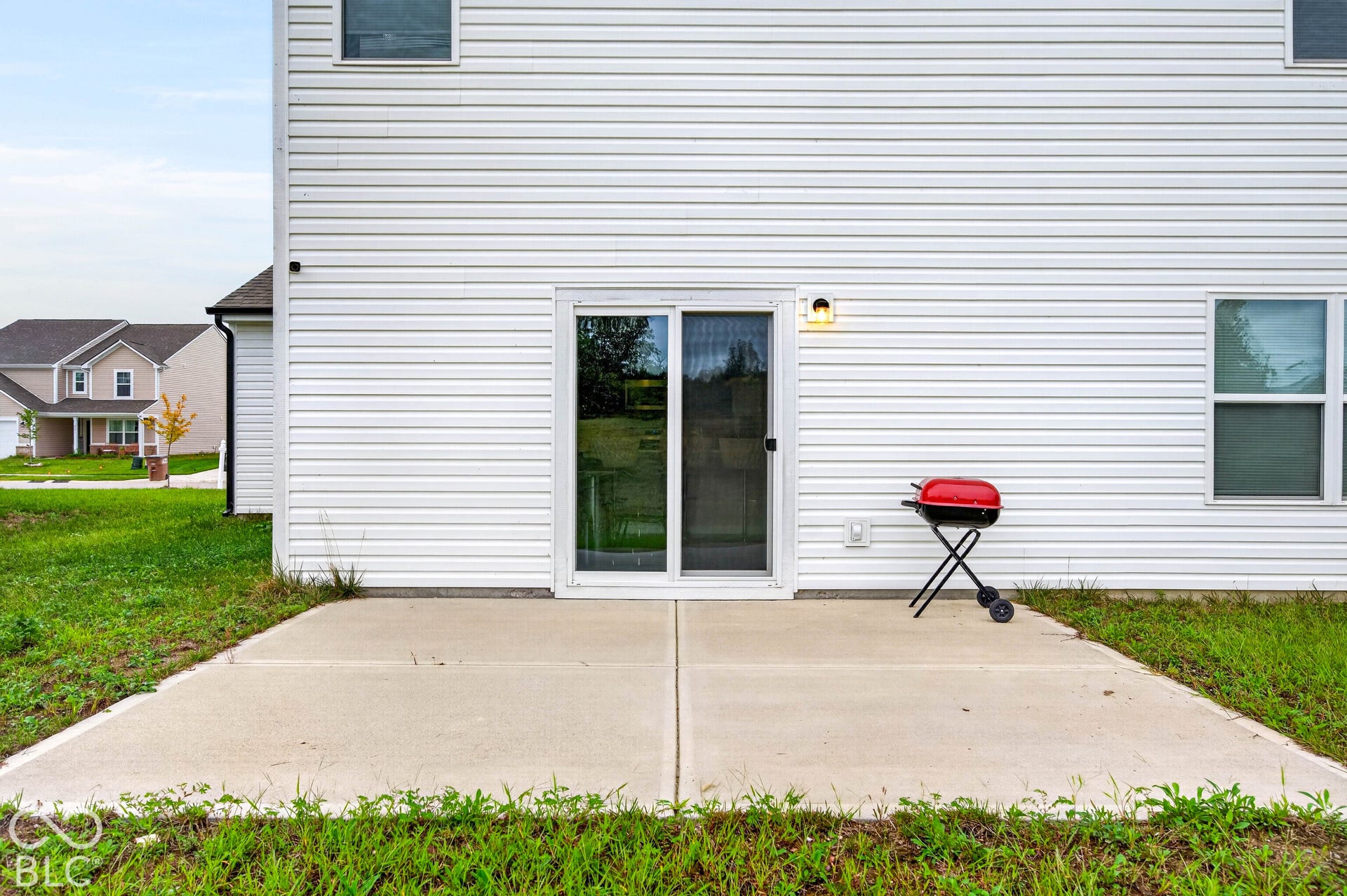 Concrete patio featuring horizontal vinyl siding, sliding glass doors, and an exterior wall-mounted light fixture